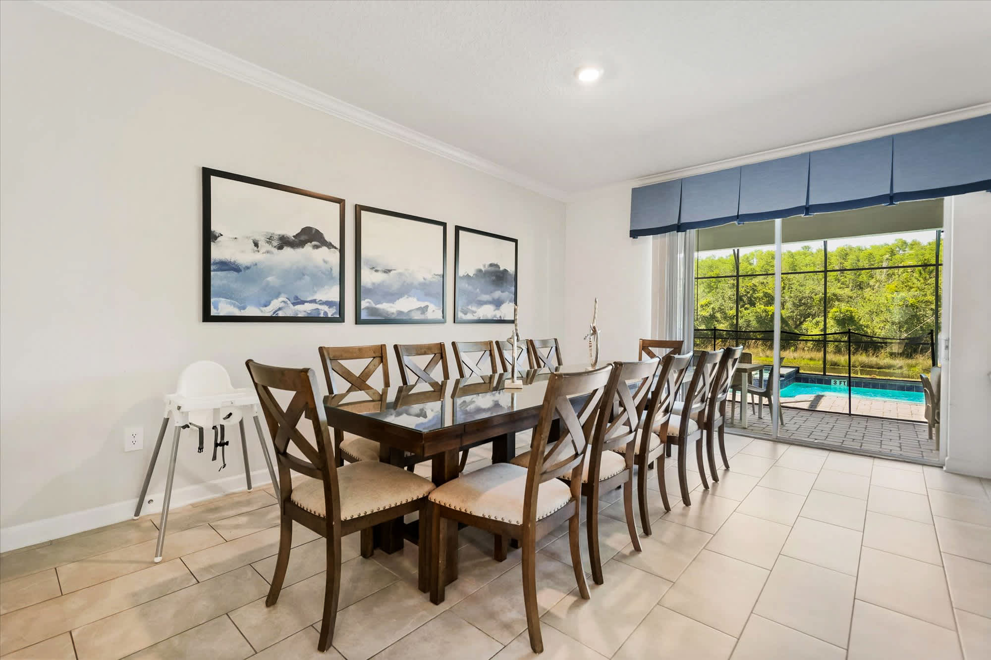 Private dining room with seating for 12, framed mountain artwork, and sliding glass doors opening to the screened pool and wooded surroundings.