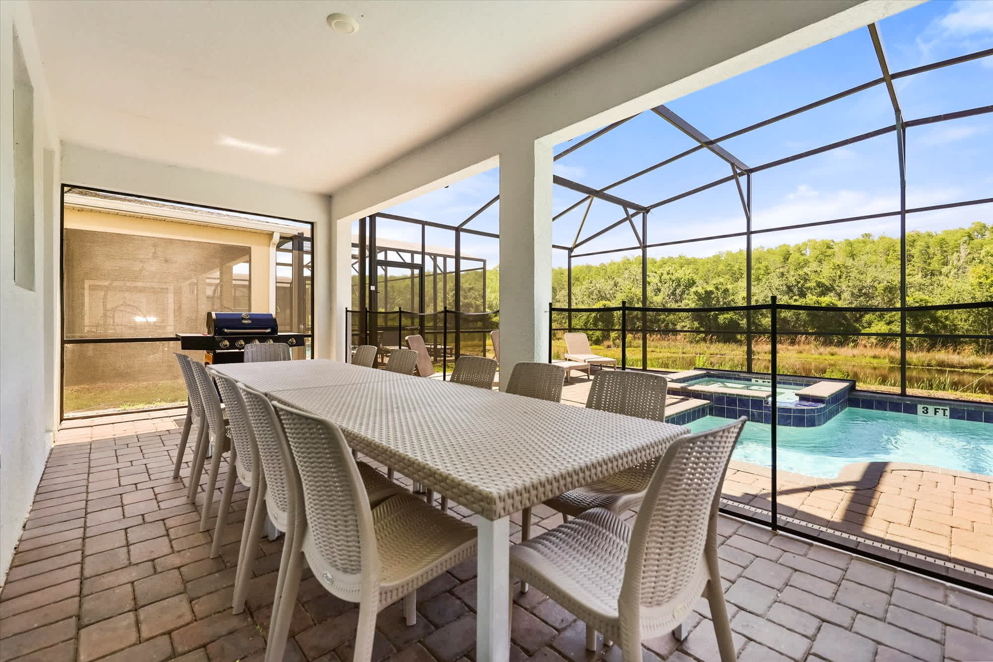 Covered poolside patio with a large outdoor dining table, gas grill, screened pool and spa, and peaceful wooded views for memorable group meals outdoors.