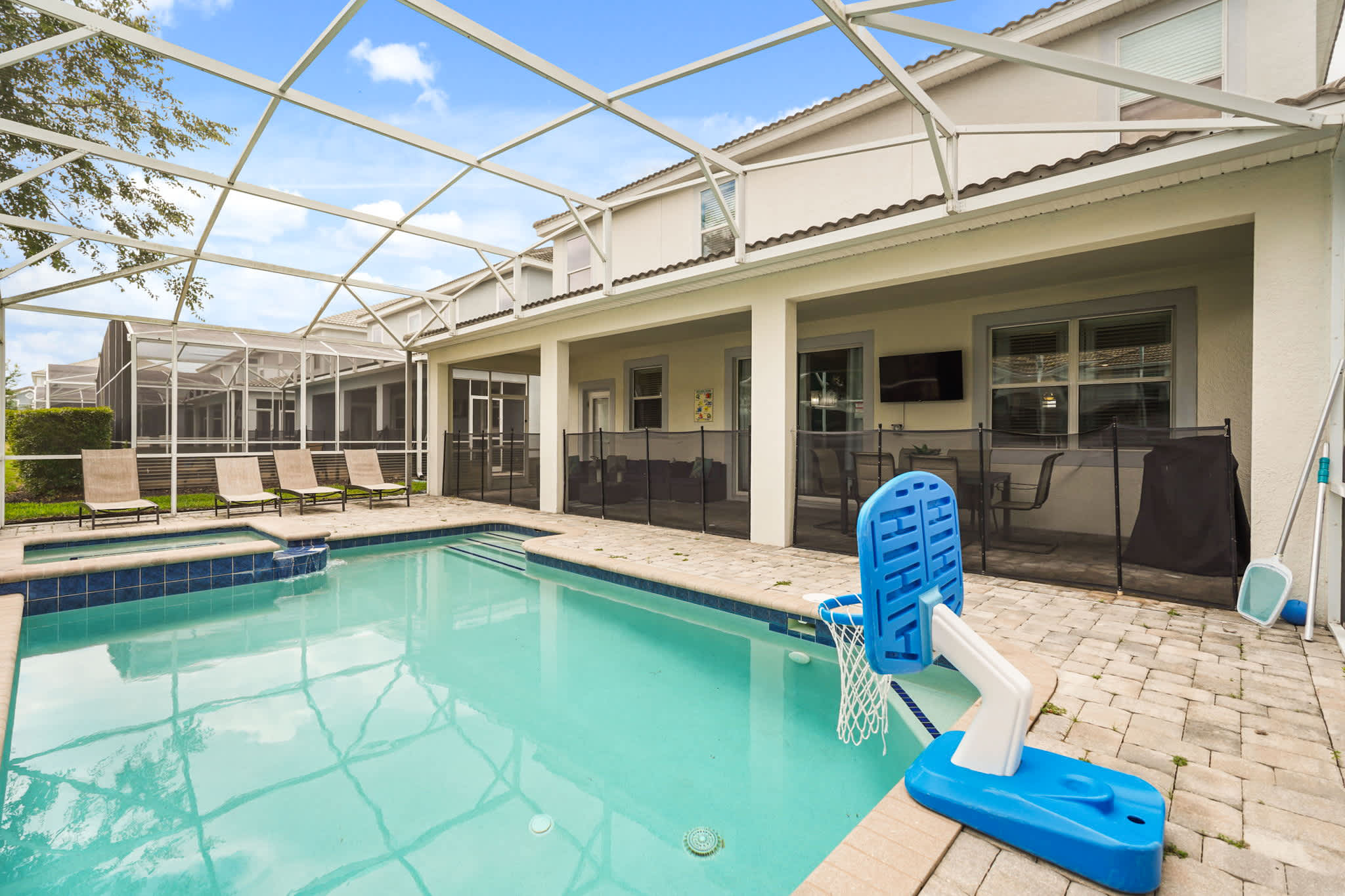 Private screened pool courtyard with a raised spa, waterslide, floating basketball hoop, loungers, and covered patio seating for sunny group fun.