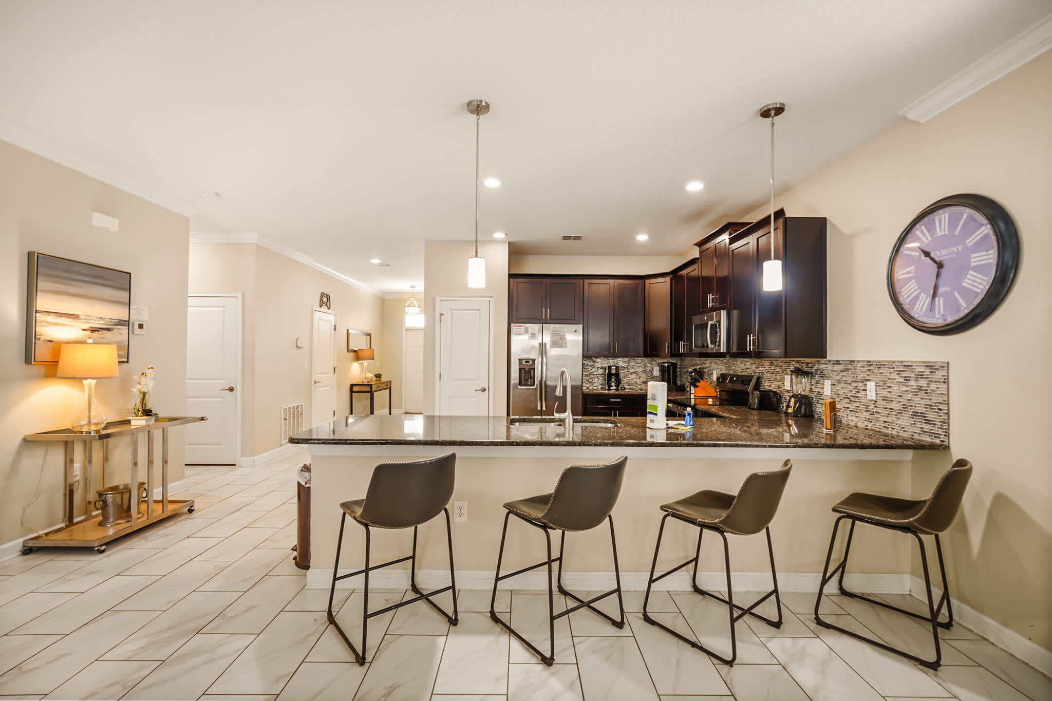 Spacious kitchen with a granite island, four bar stools, dark wood cabinetry, stainless appliances, and a textured mosaic backsplash for group meals.