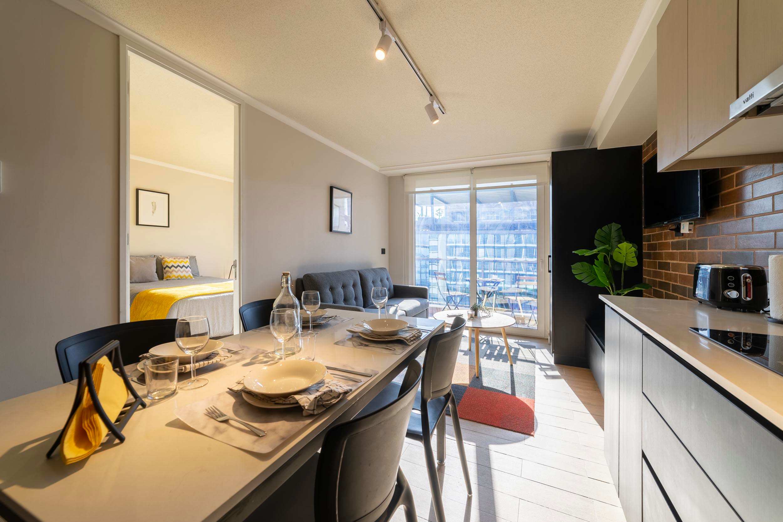 Bright and modern living space with a cozy sofa and dining area, leading to a sunlit balcony perfect for relaxation.