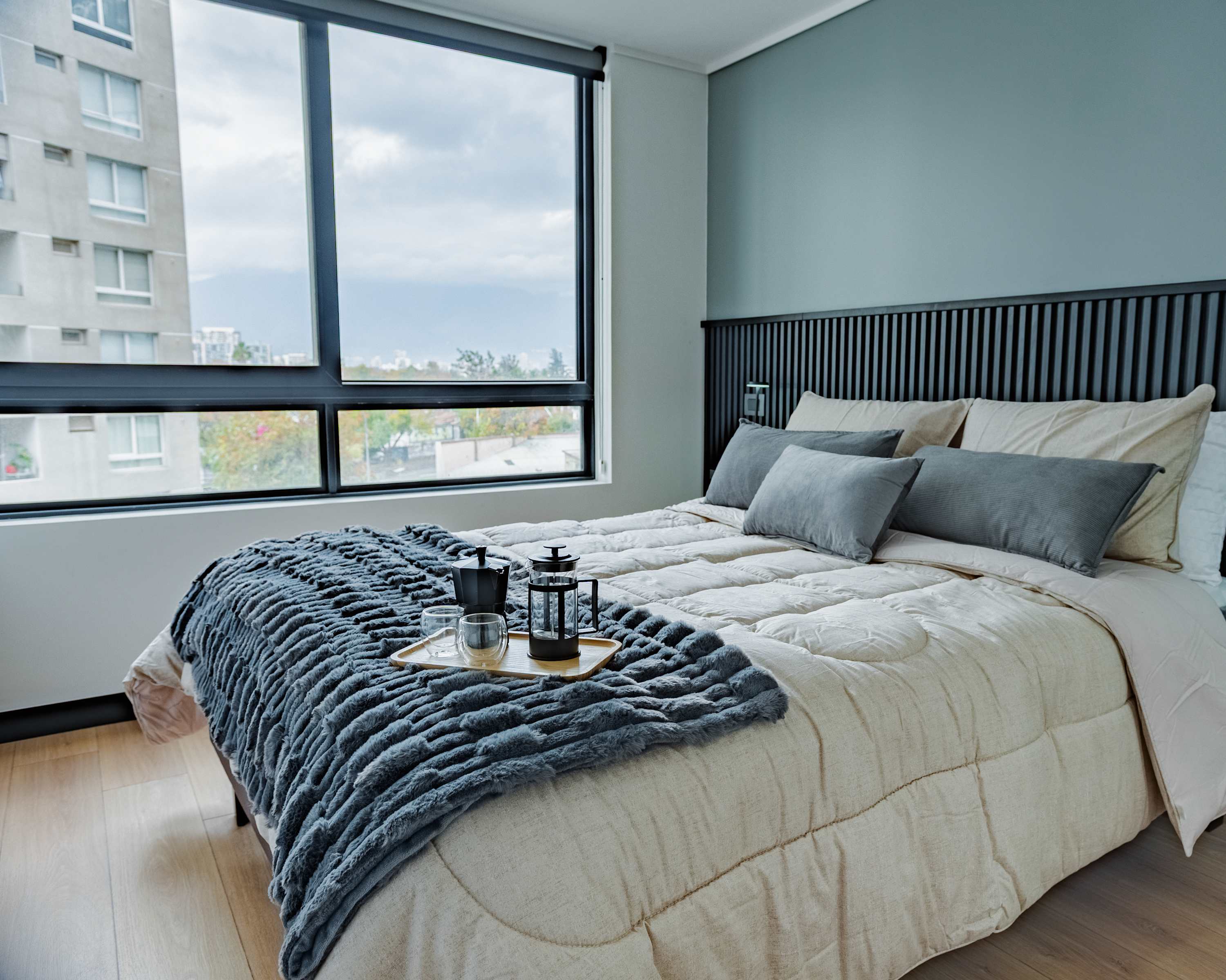 Relax in this stylish bedroom with a city view, featuring cozy bedding and modern decor.