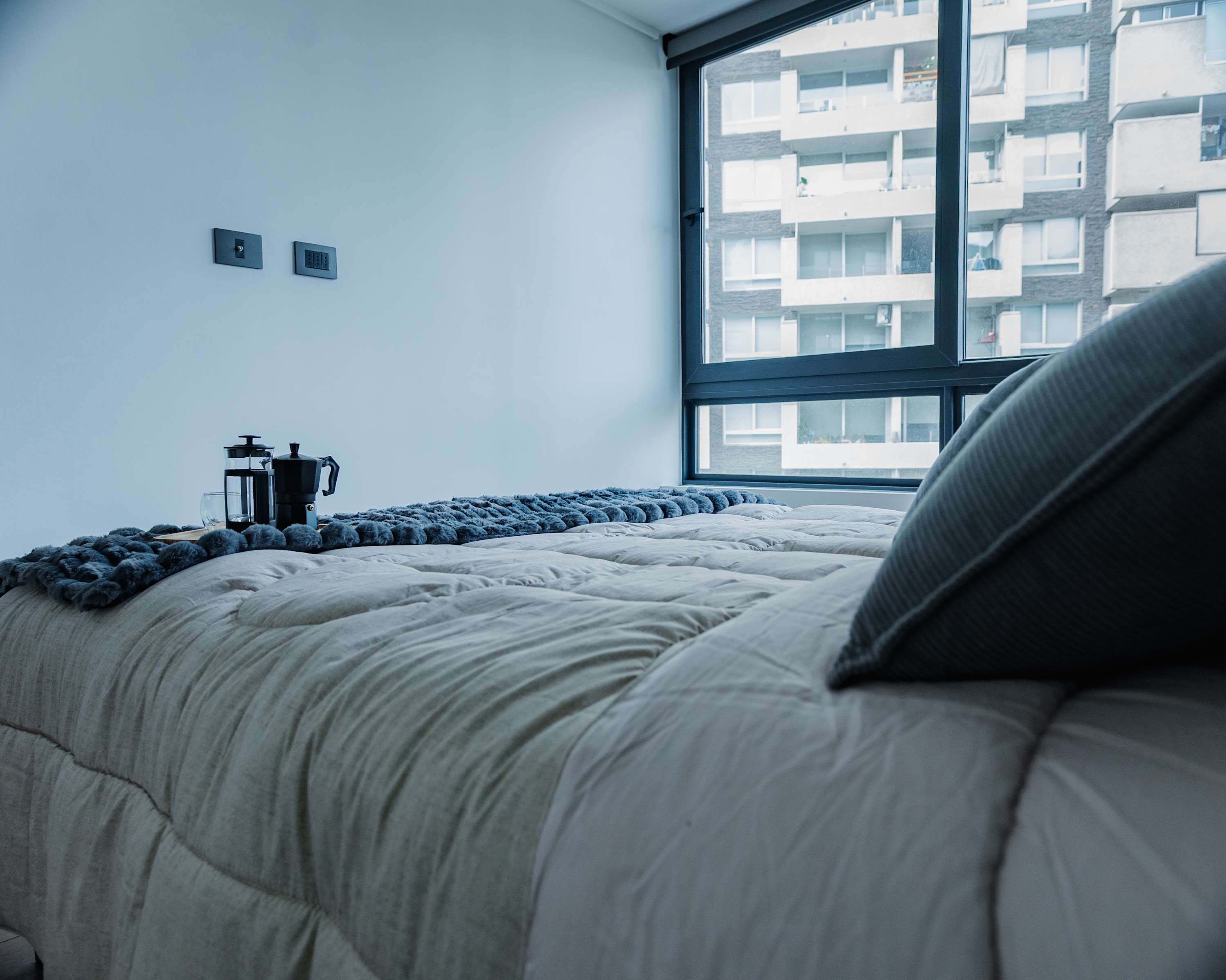 Cozy bedroom with a large window offering city views, perfect for a relaxing stay.