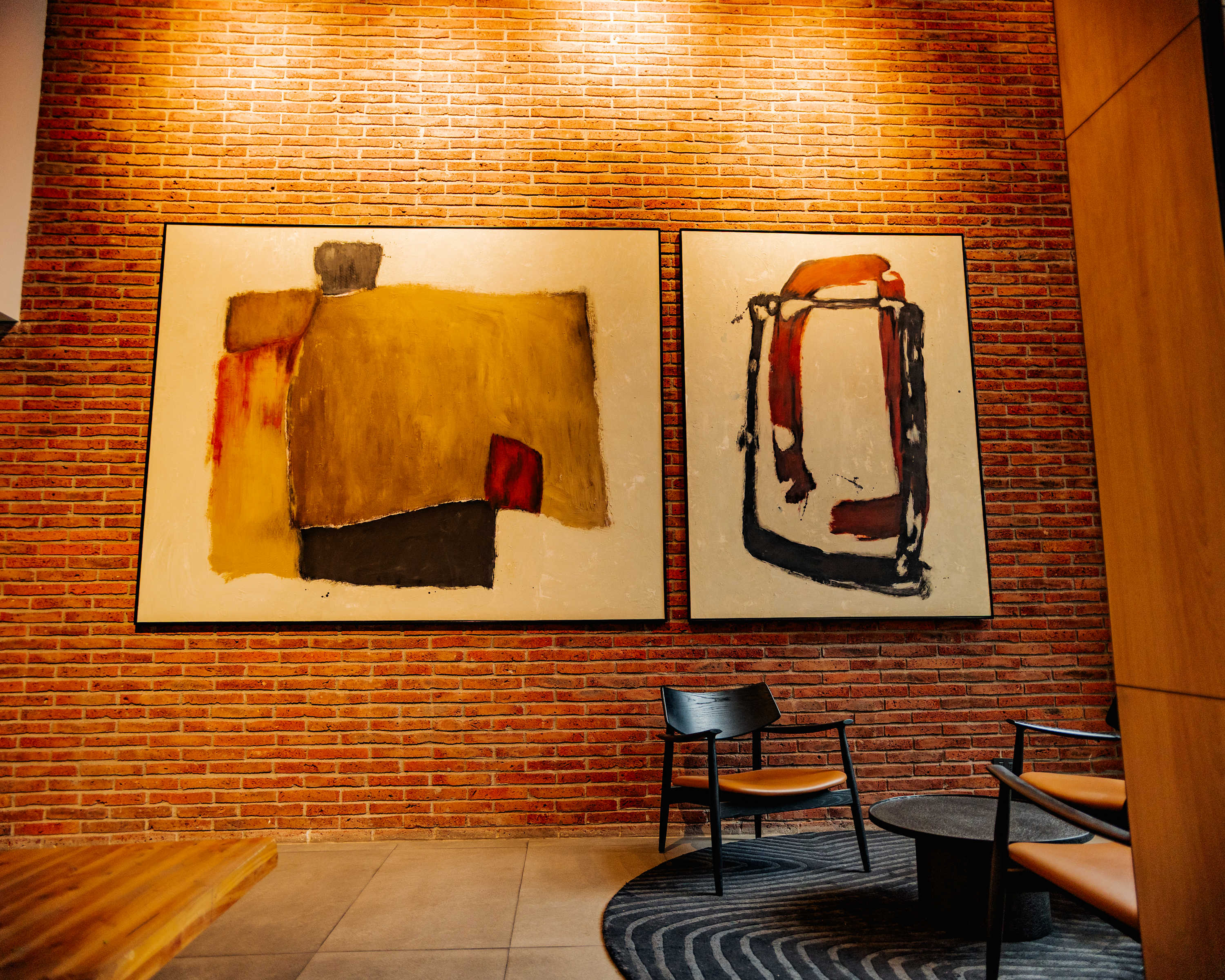 Private living room with an exposed brick accent wall, abstract artwork, leather lounge chairs, and a patterned rug.