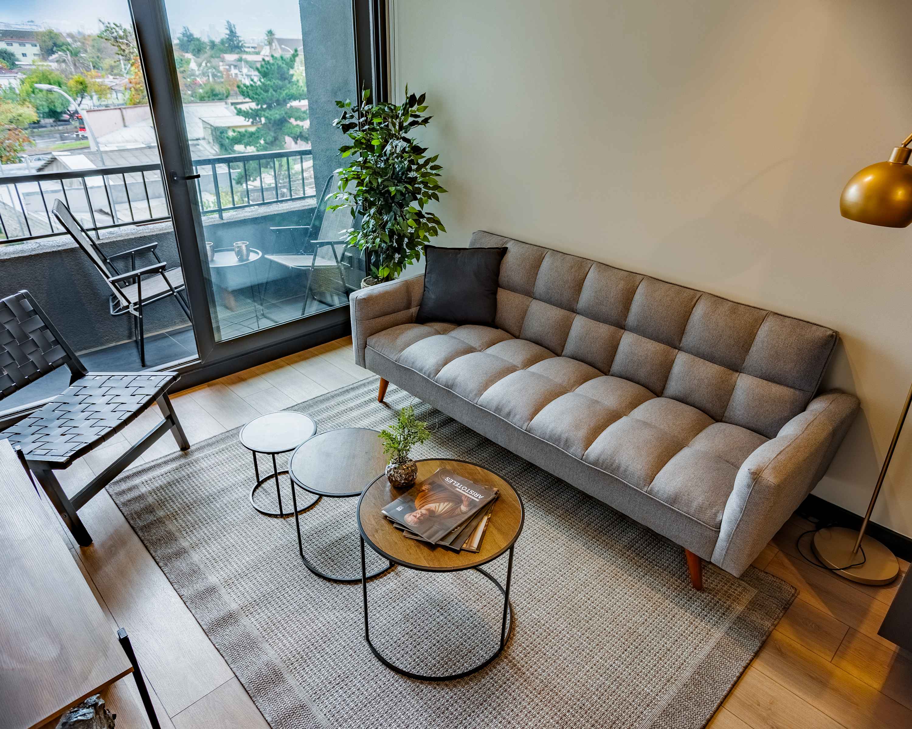 Relax in the stylish living room with a spacious gray sectional, curated coffee tables, and glass doors opening to a furnished private balcony with leafy neighborhood views.