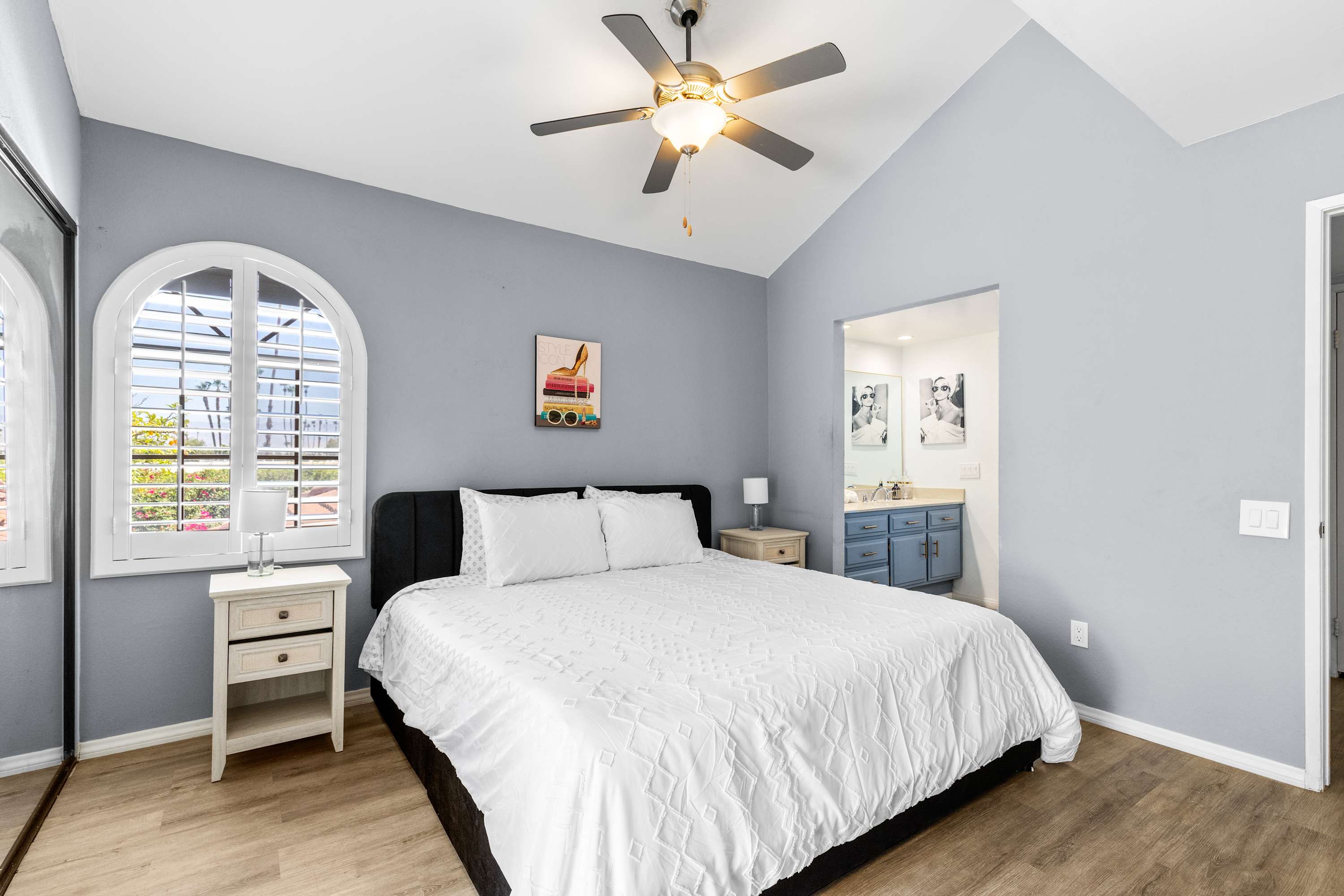 Wide bedroom view with gray walls, ceiling fan and adjoining vanity area.