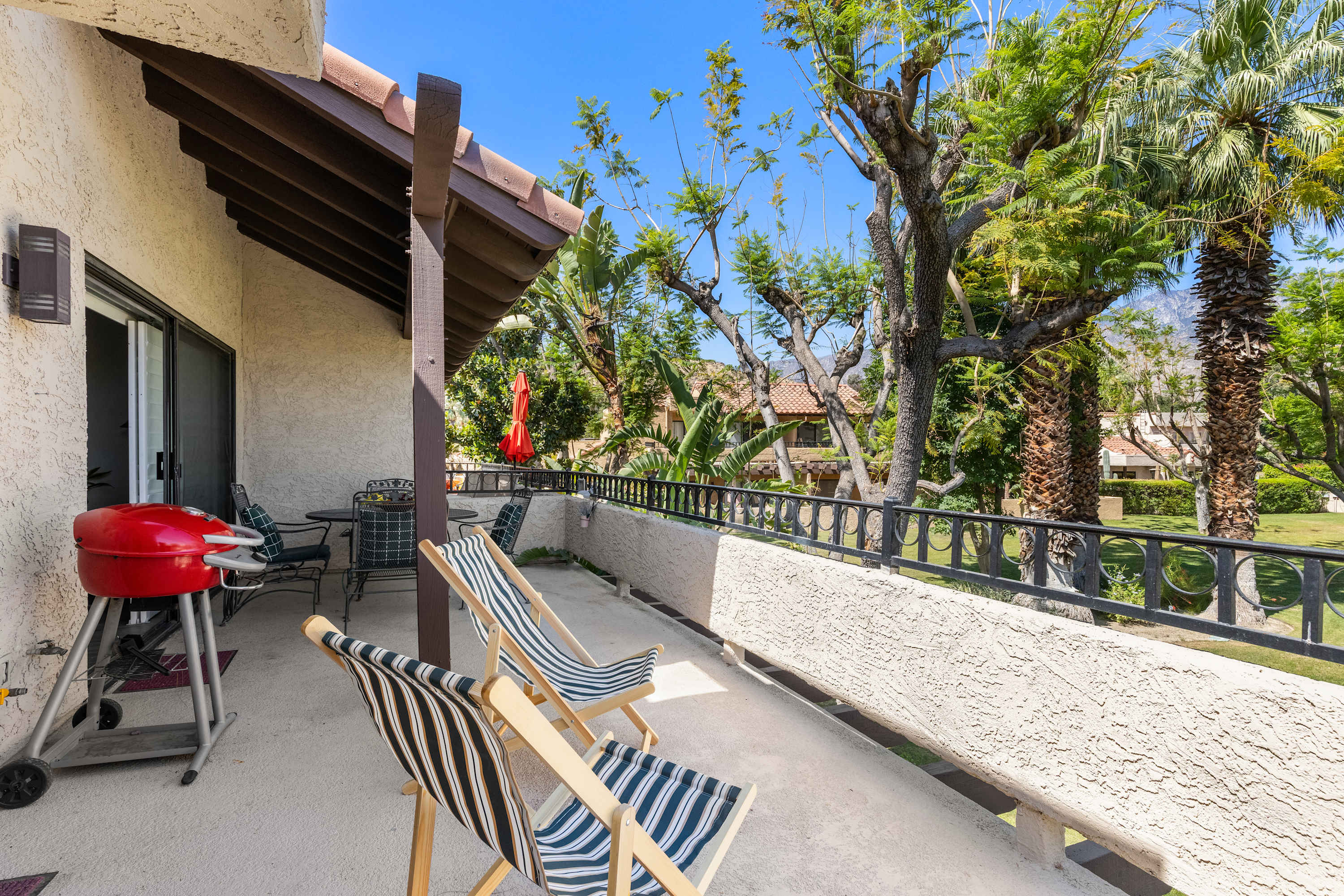 Wide balcony view with striped chairs, a grill and sliding doors.