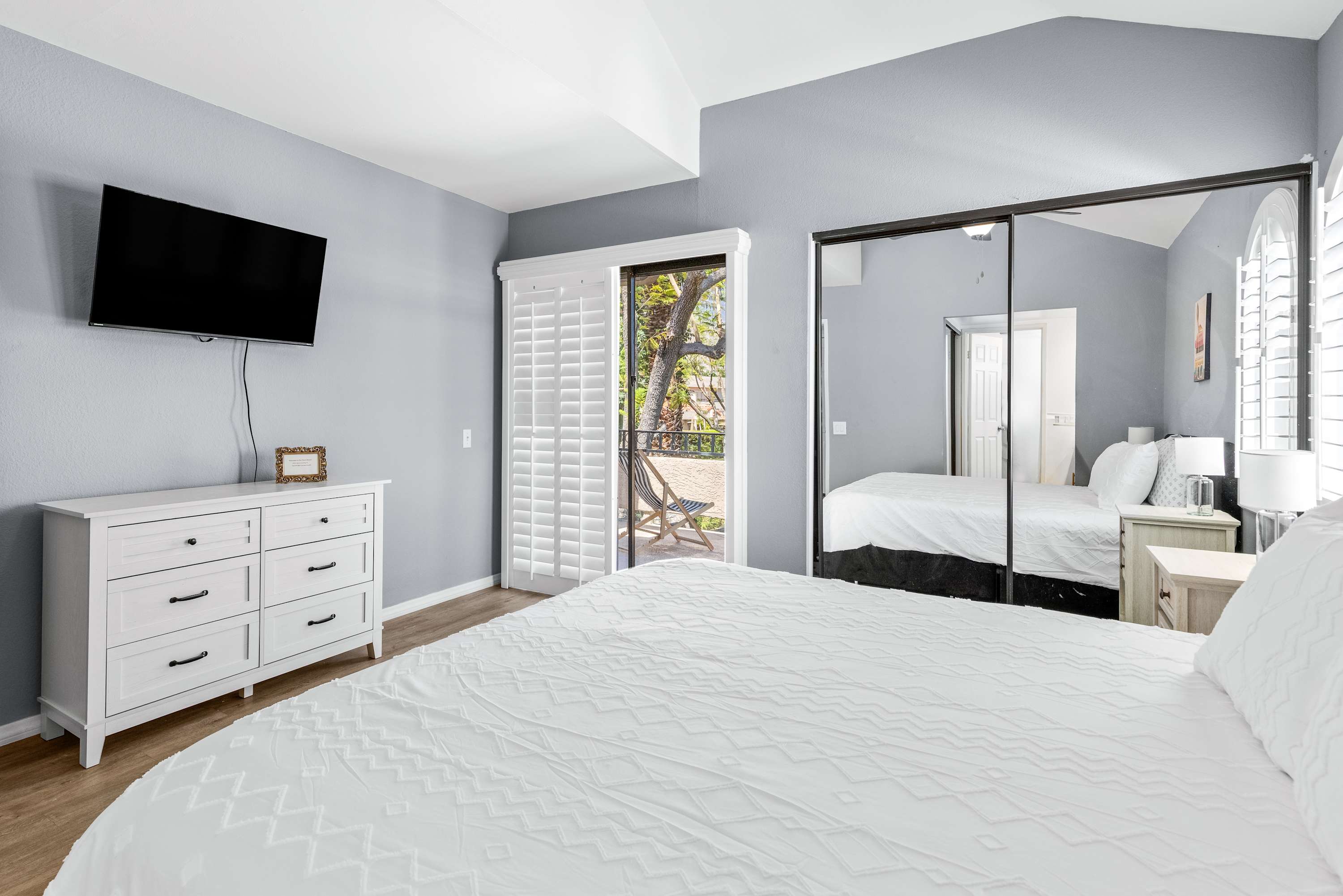 Bedroom with a dresser, wall-mounted TV and mirrored closet doors.