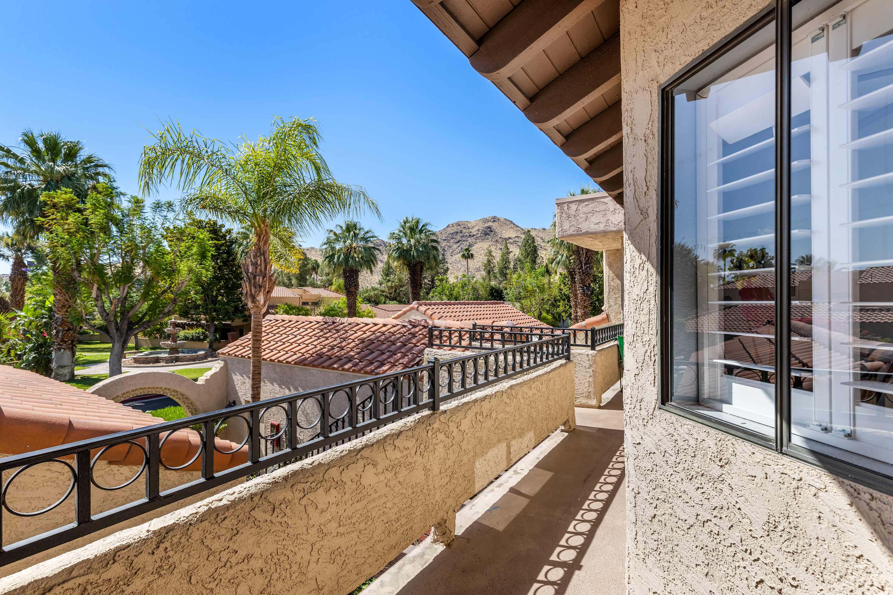 Balcony view over the railing toward nearby rooftops, palms and mountains.