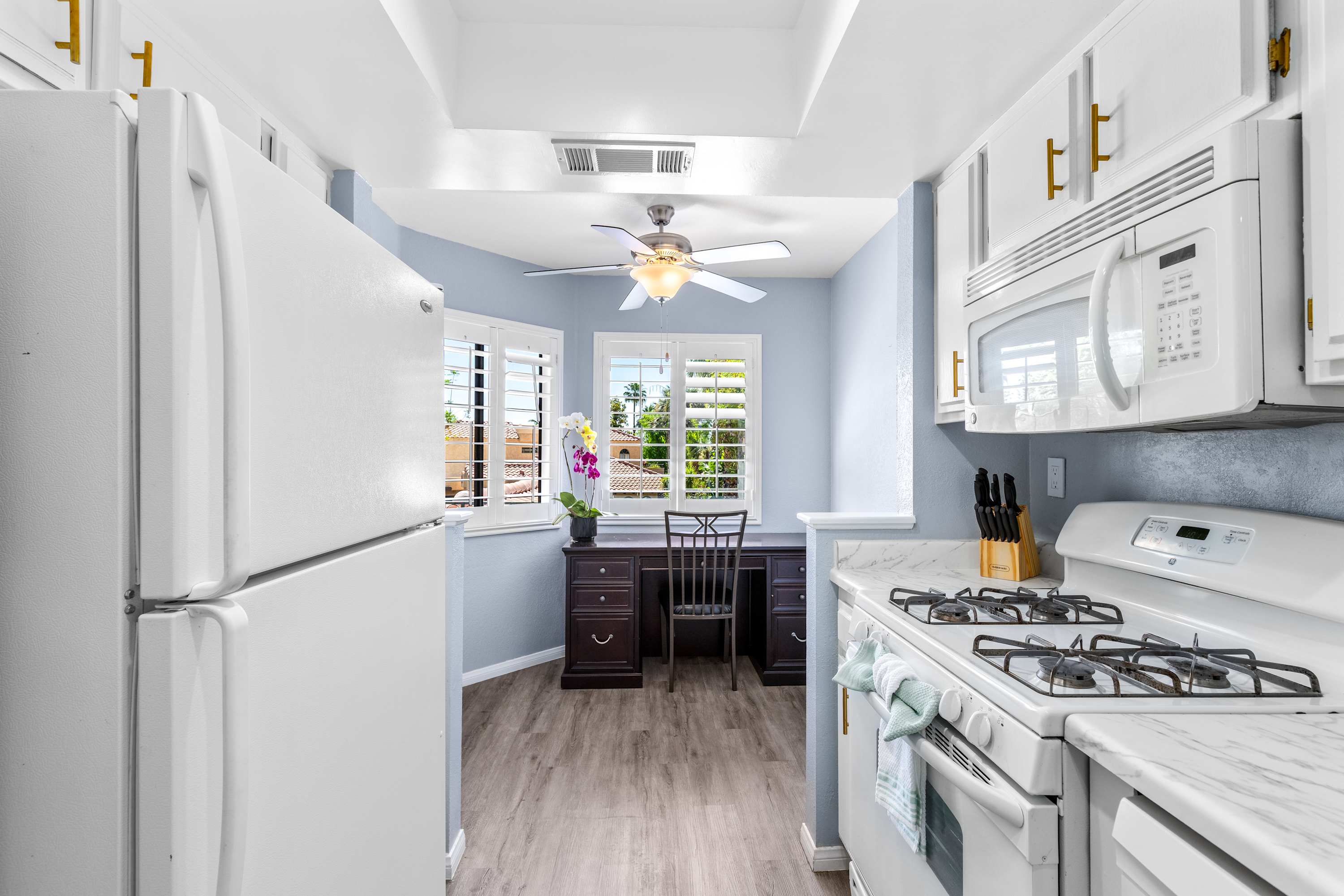 Galley kitchen with a refrigerator, gas range and window at the far end.