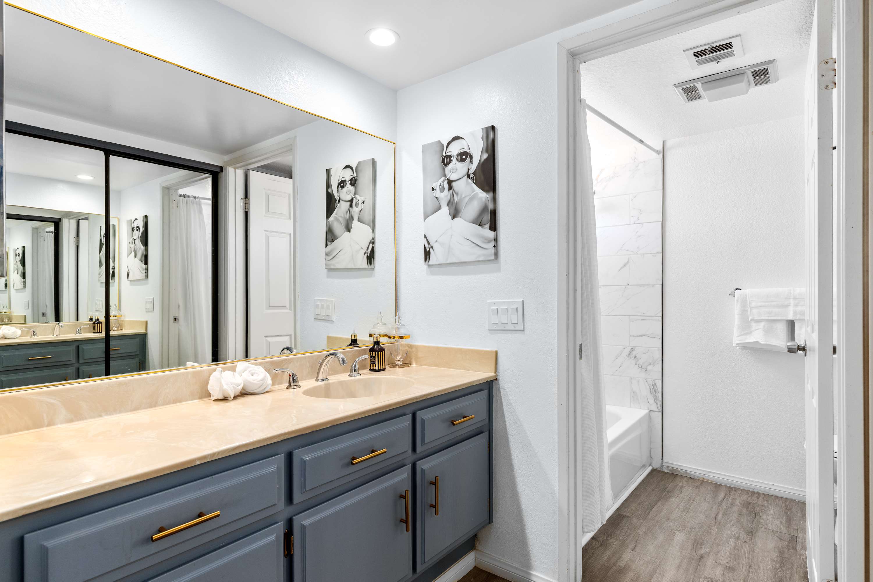 Bathroom with a double vanity, large mirror, gray cabinets and framed artwork.