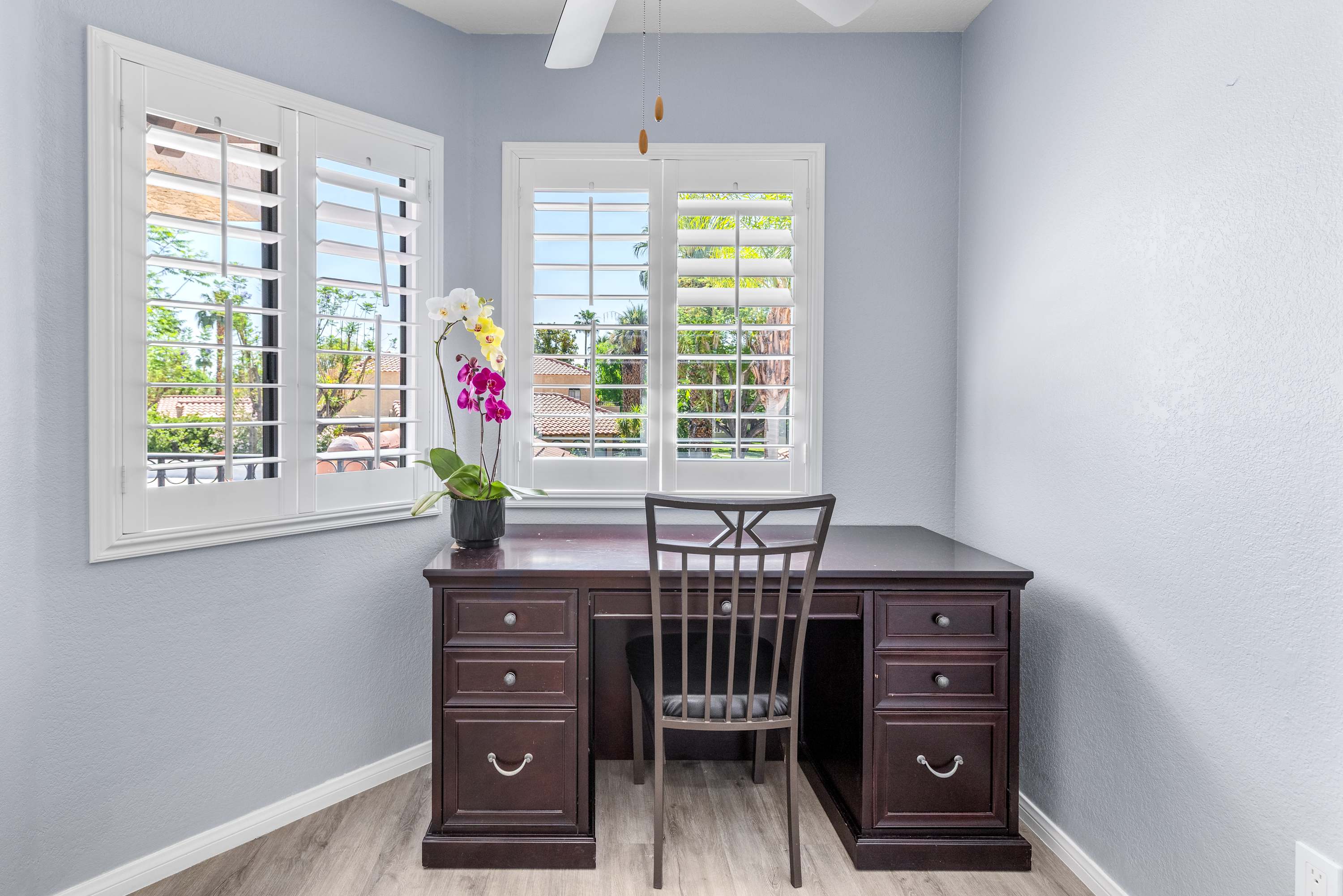 Wood desk and chair in a bright corner with shuttered windows.