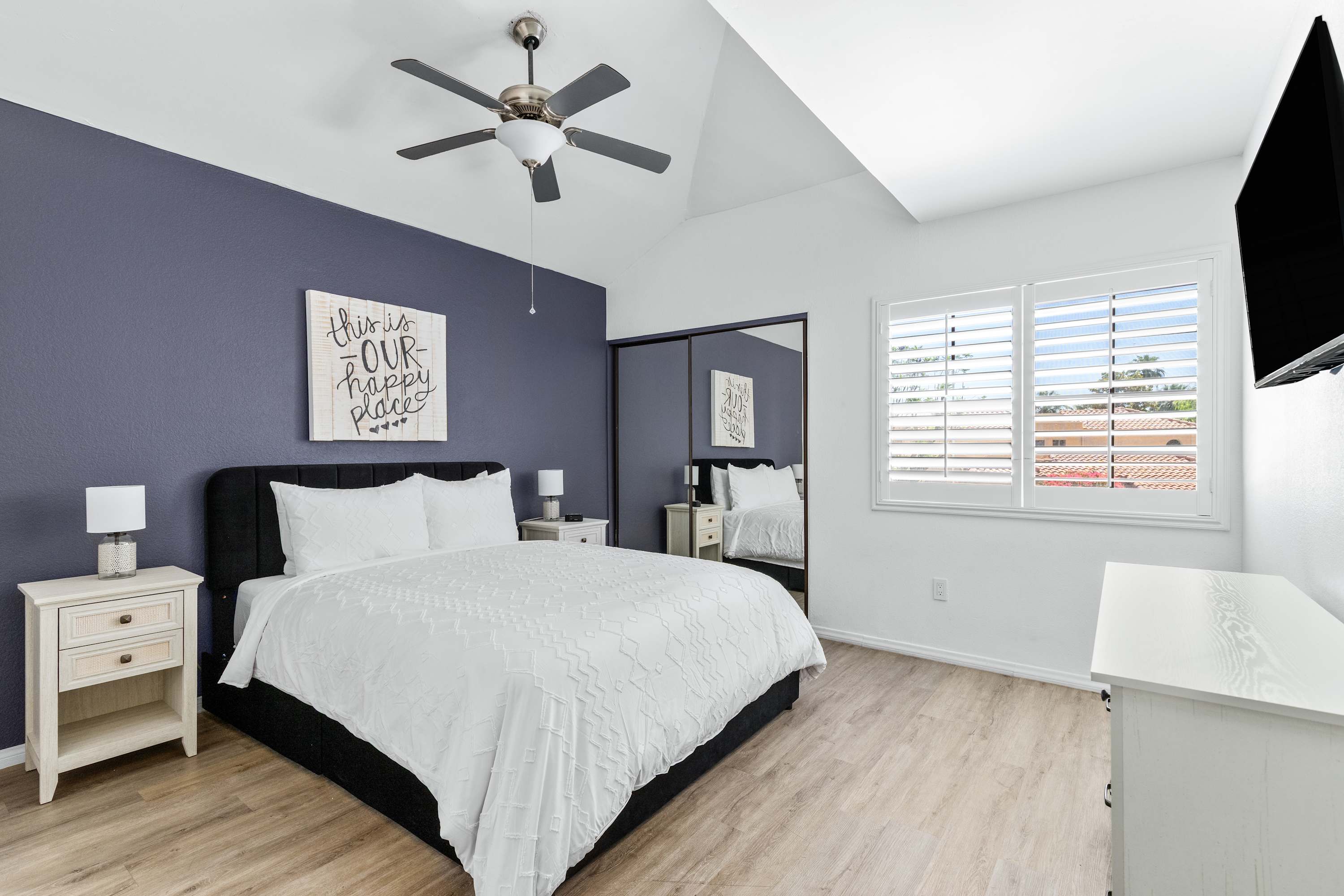 Bedroom with a dark accent wall, white bedding, ceiling fan and dresser.