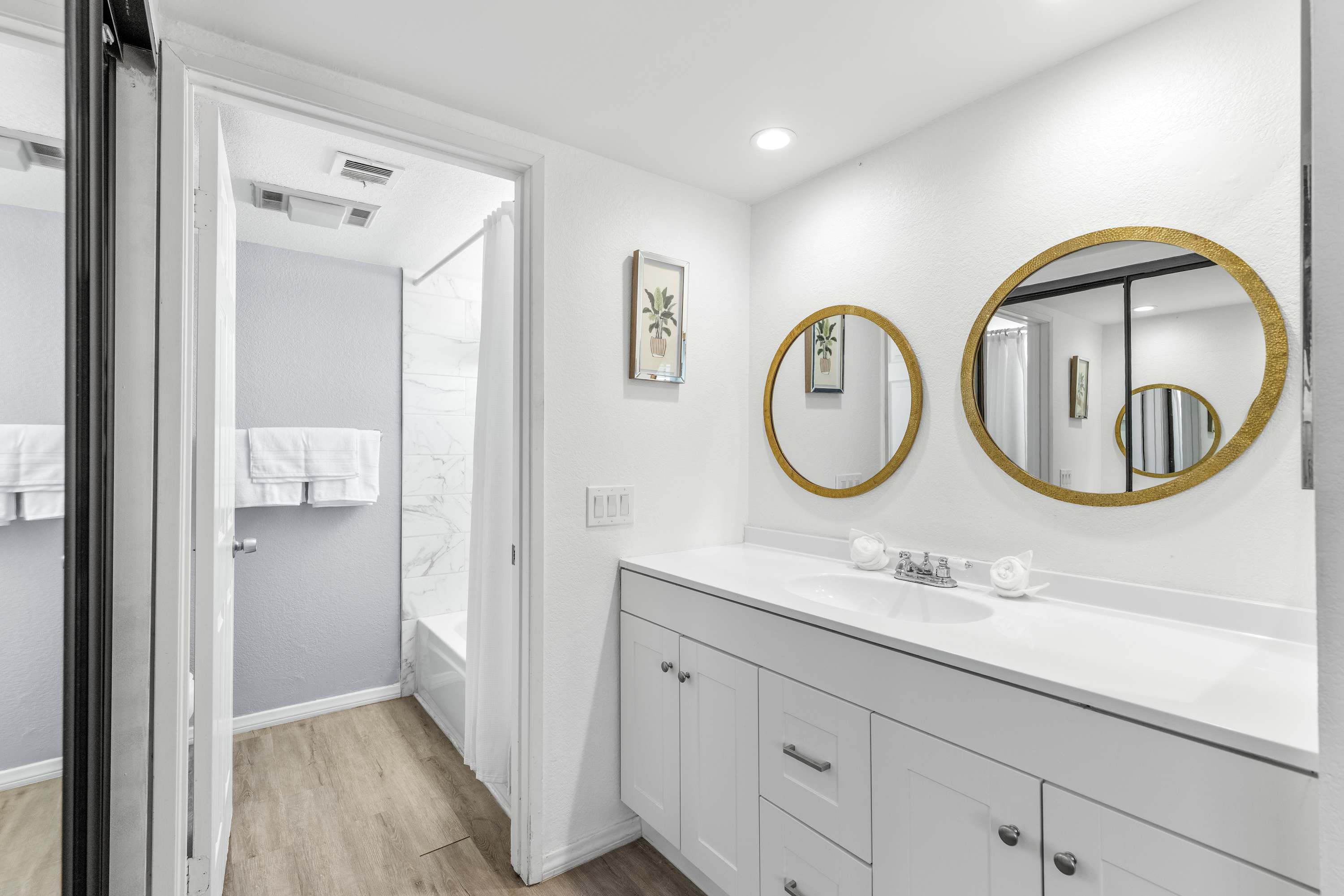 Bathroom with white vanity cabinets, round mirrors and a shuttered window.