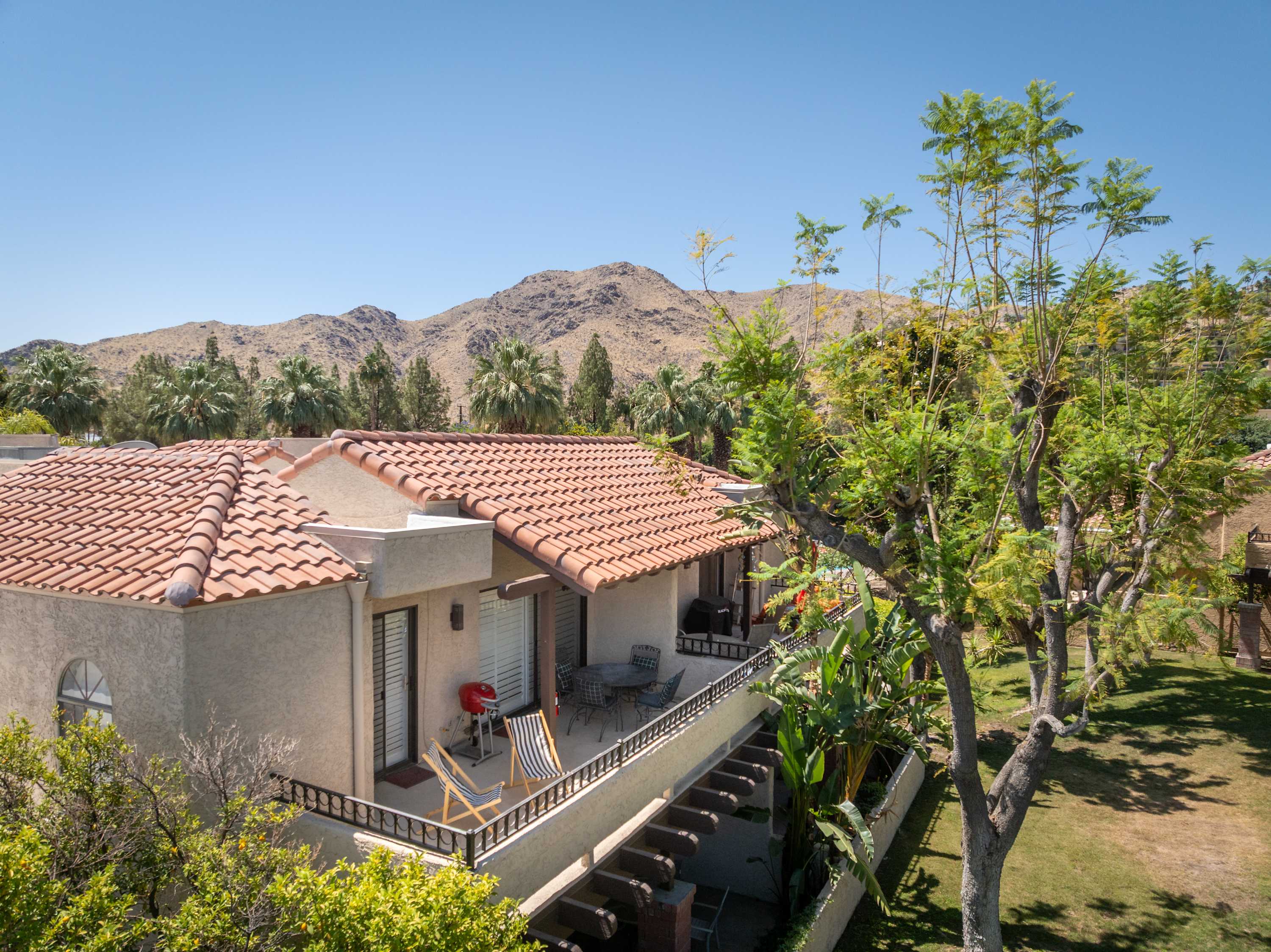 Aerial building view with tiled roofs, palms and mountains beyond.