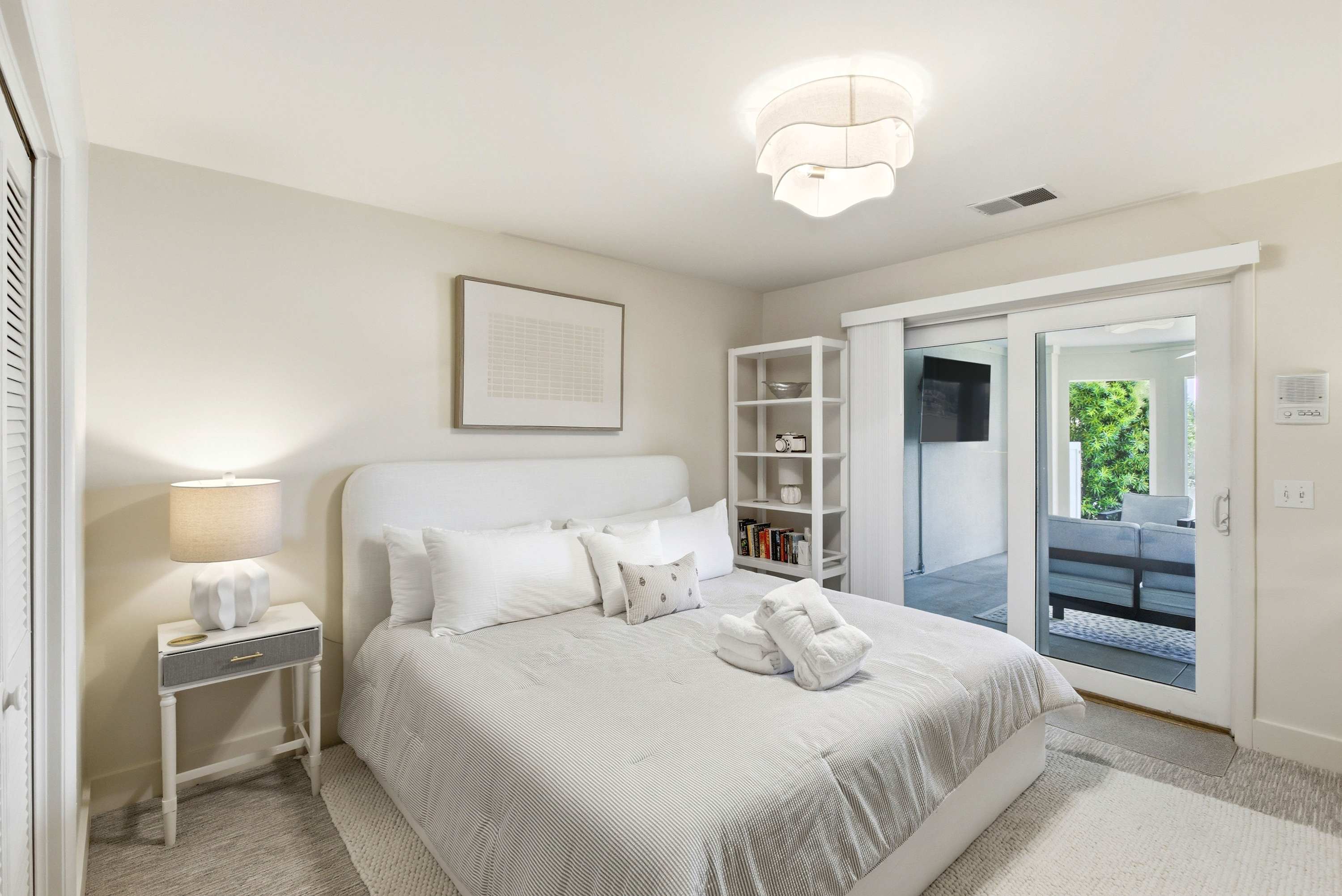 King suite with plush upholstered headboard, private patio access, dedicated bookshelf, and soft natural light.