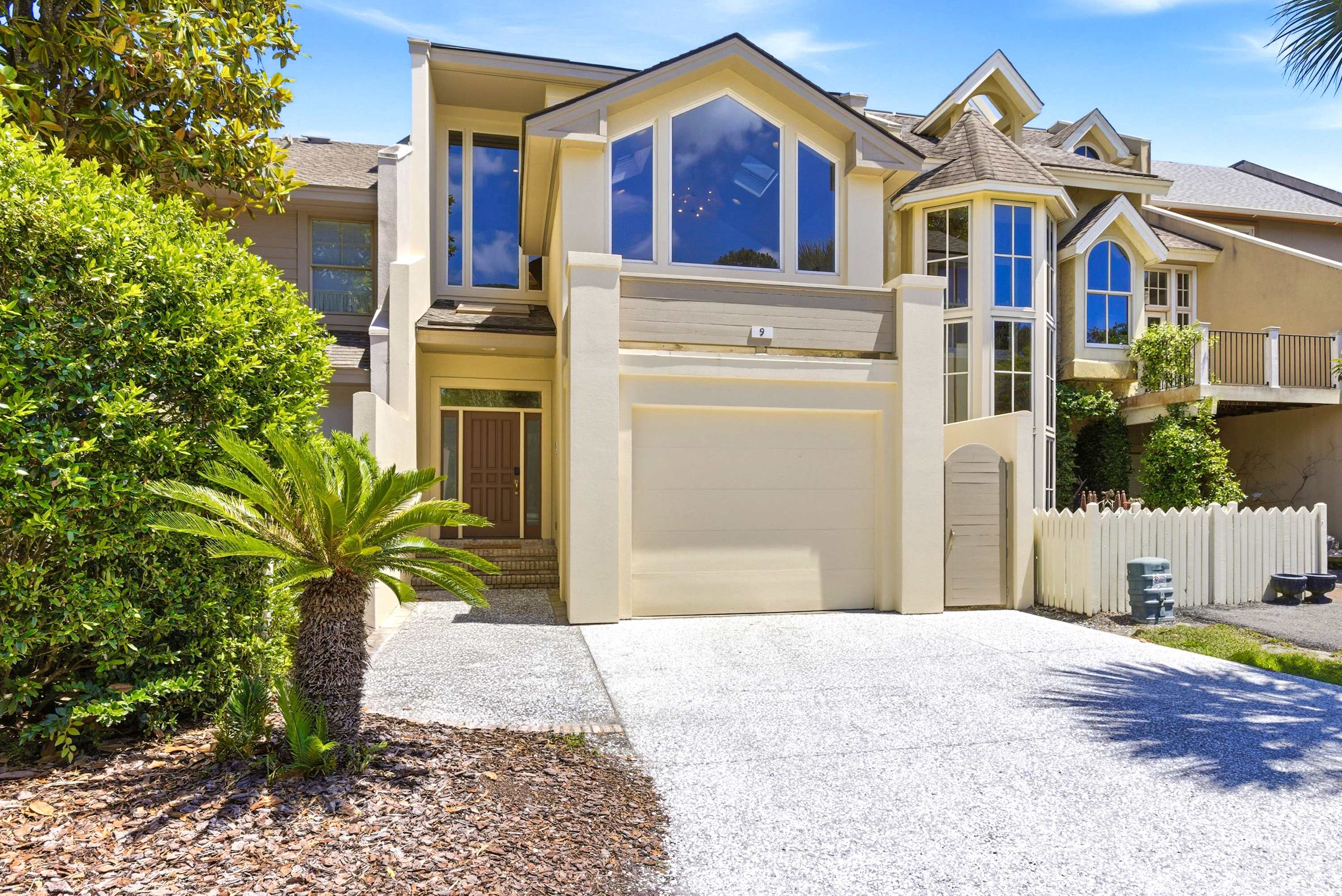 Dramatic facade with oversized picture windows, manicured tropical grounds, and a wide private driveway.