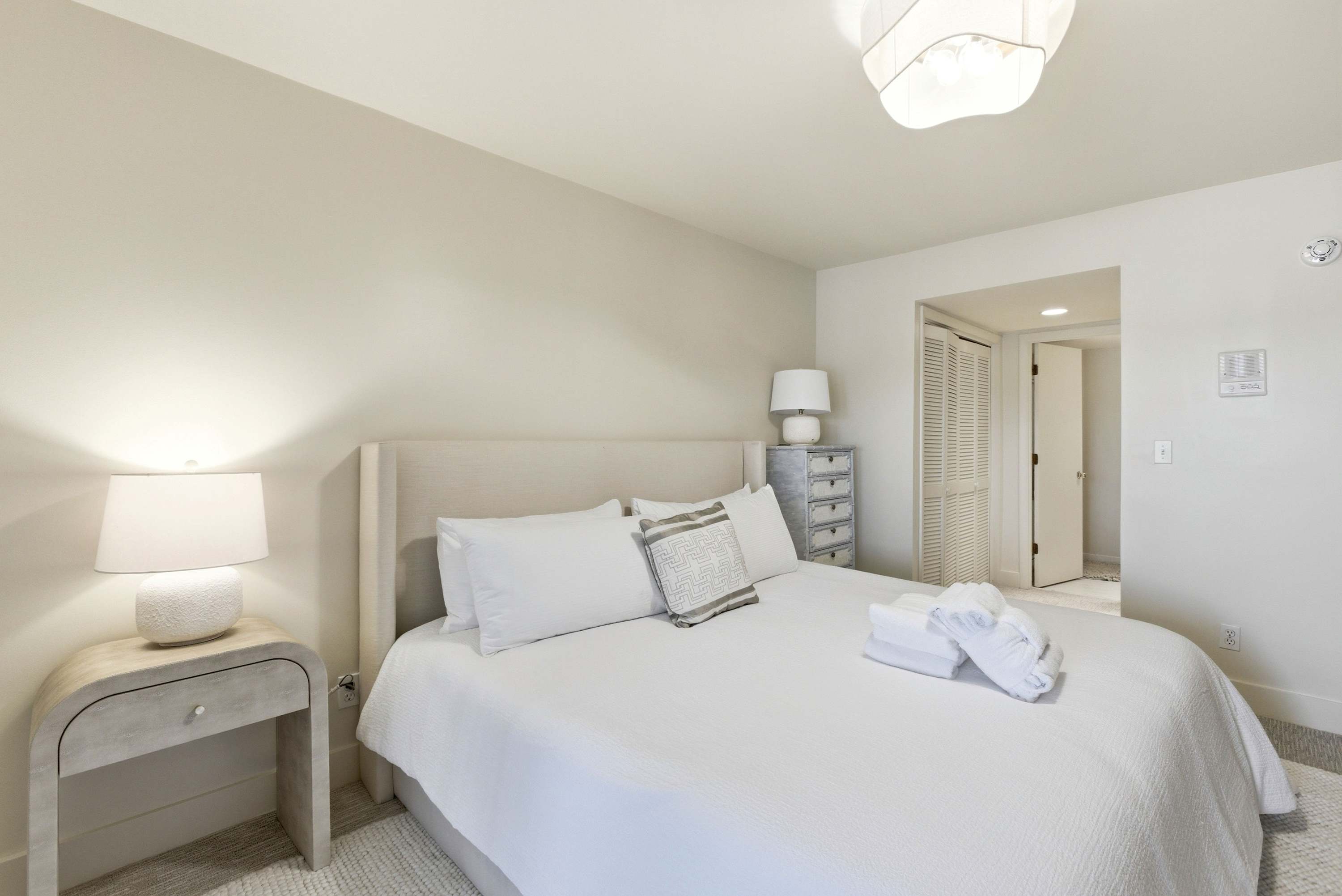 King bedroom dressed in crisp white linens with custom textured nightstands and warm ambient lighting.