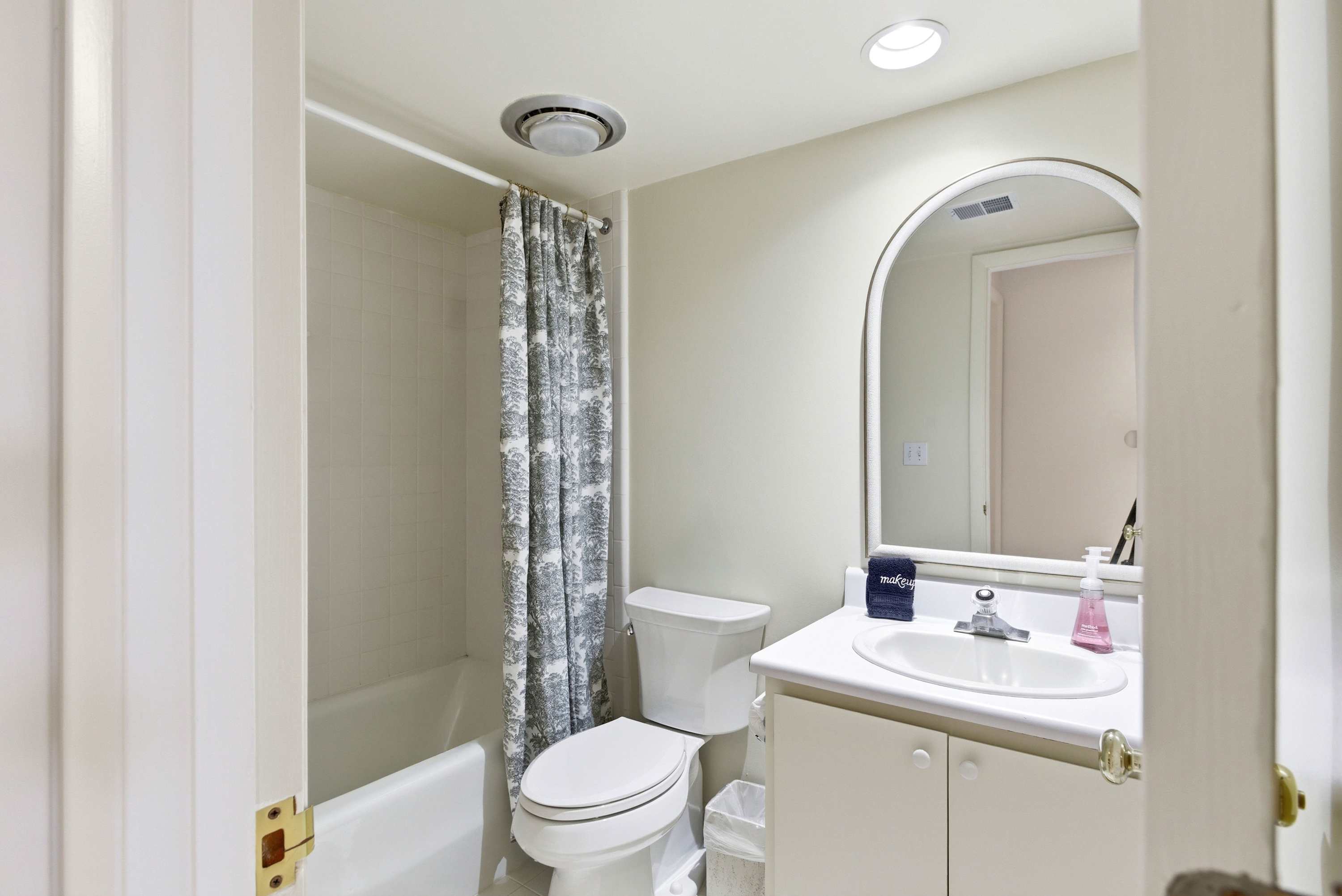 Tub and shower combo with an elegant arched mirror and boutique-hotel toiletries.