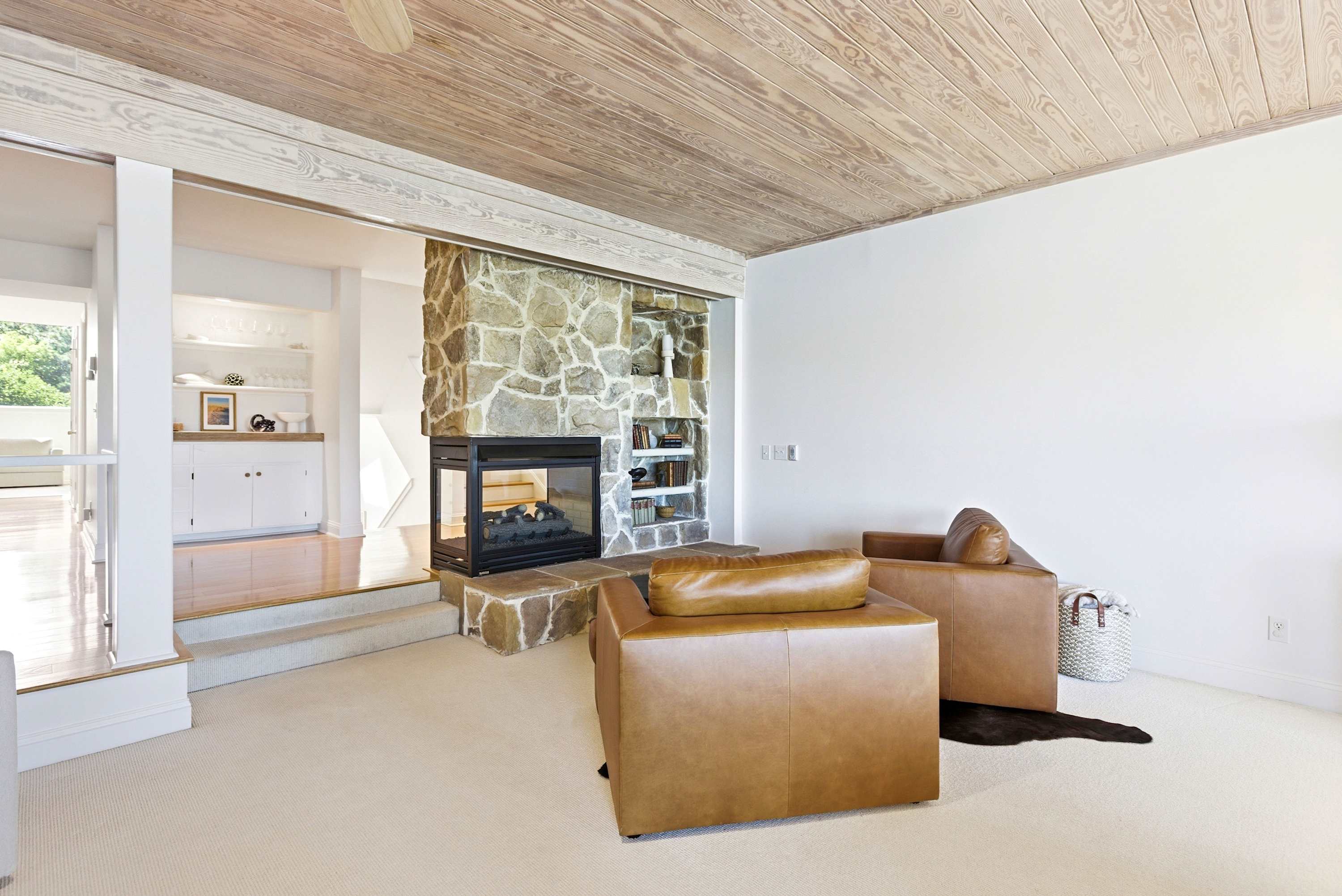 Floor-to-ceiling stone fireplace with leather lounge chairs and a wood-plank ceiling — the ideal setting for cool coastal evenings.