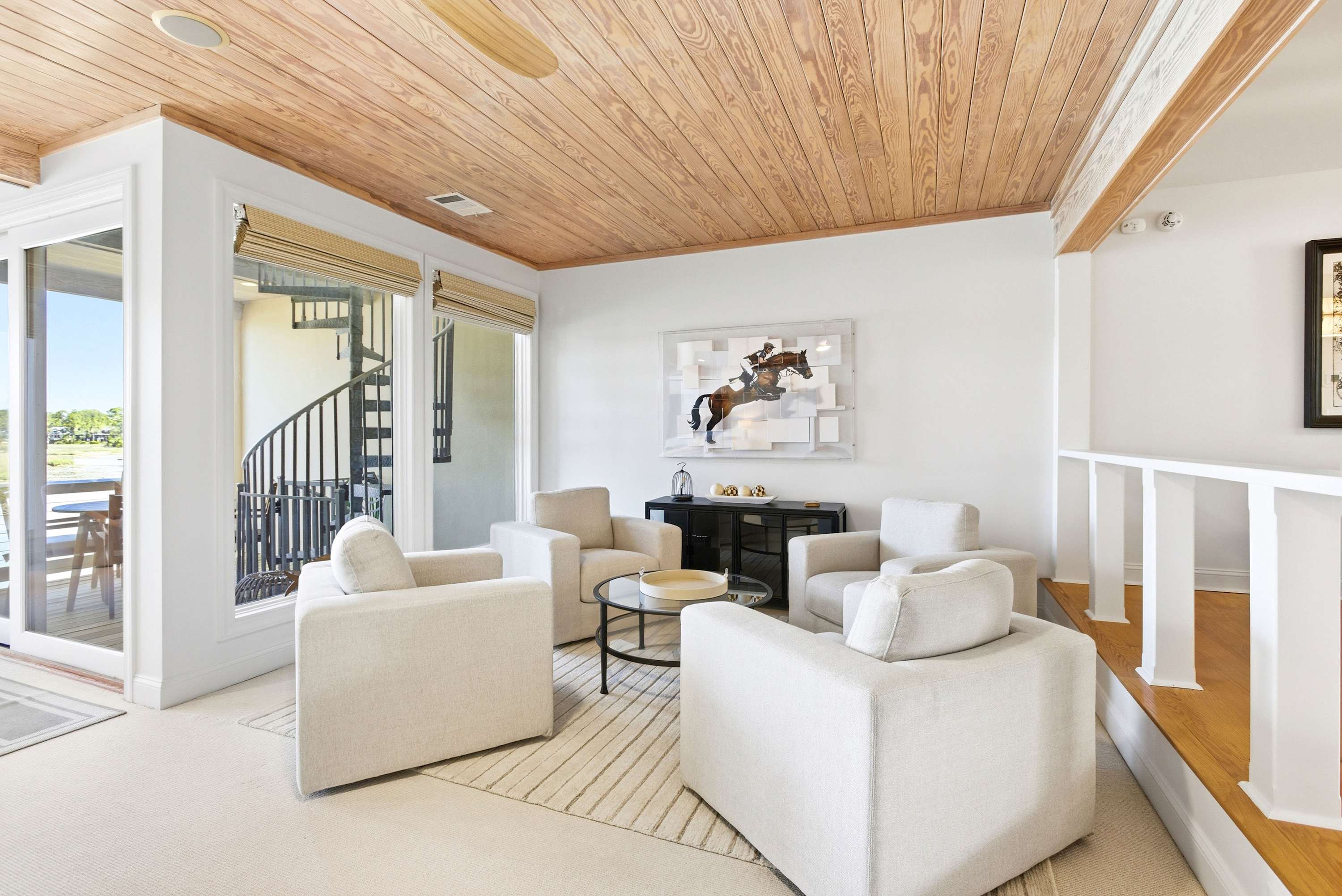 Bright upper-level sitting nook with white linen armchairs, bold equestrian art, and direct access to the upper waterfront deck.