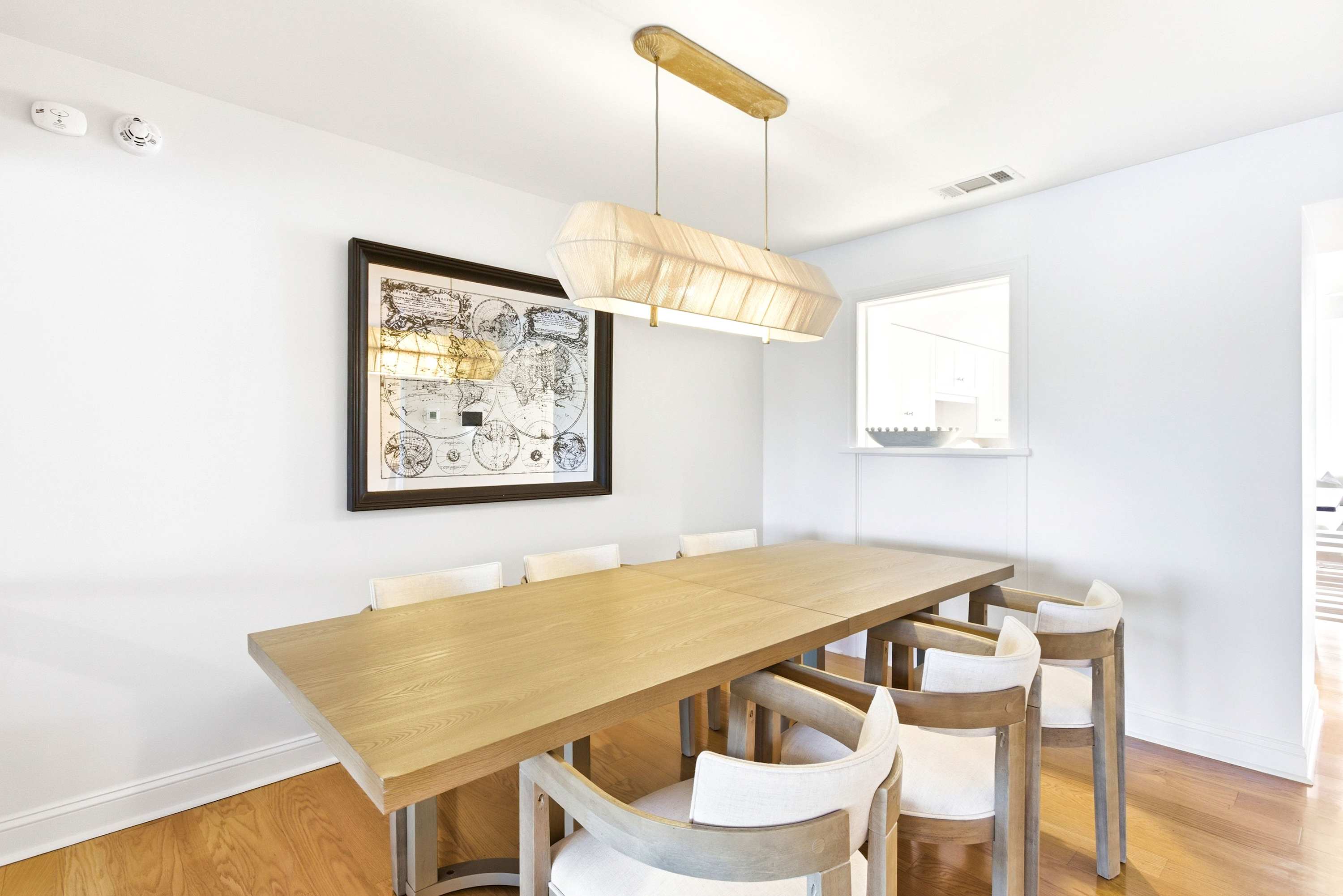 Elegant dining room with a long natural oak table, sculptural linen pendant, and vintage world map art that sets a well-traveled tone.