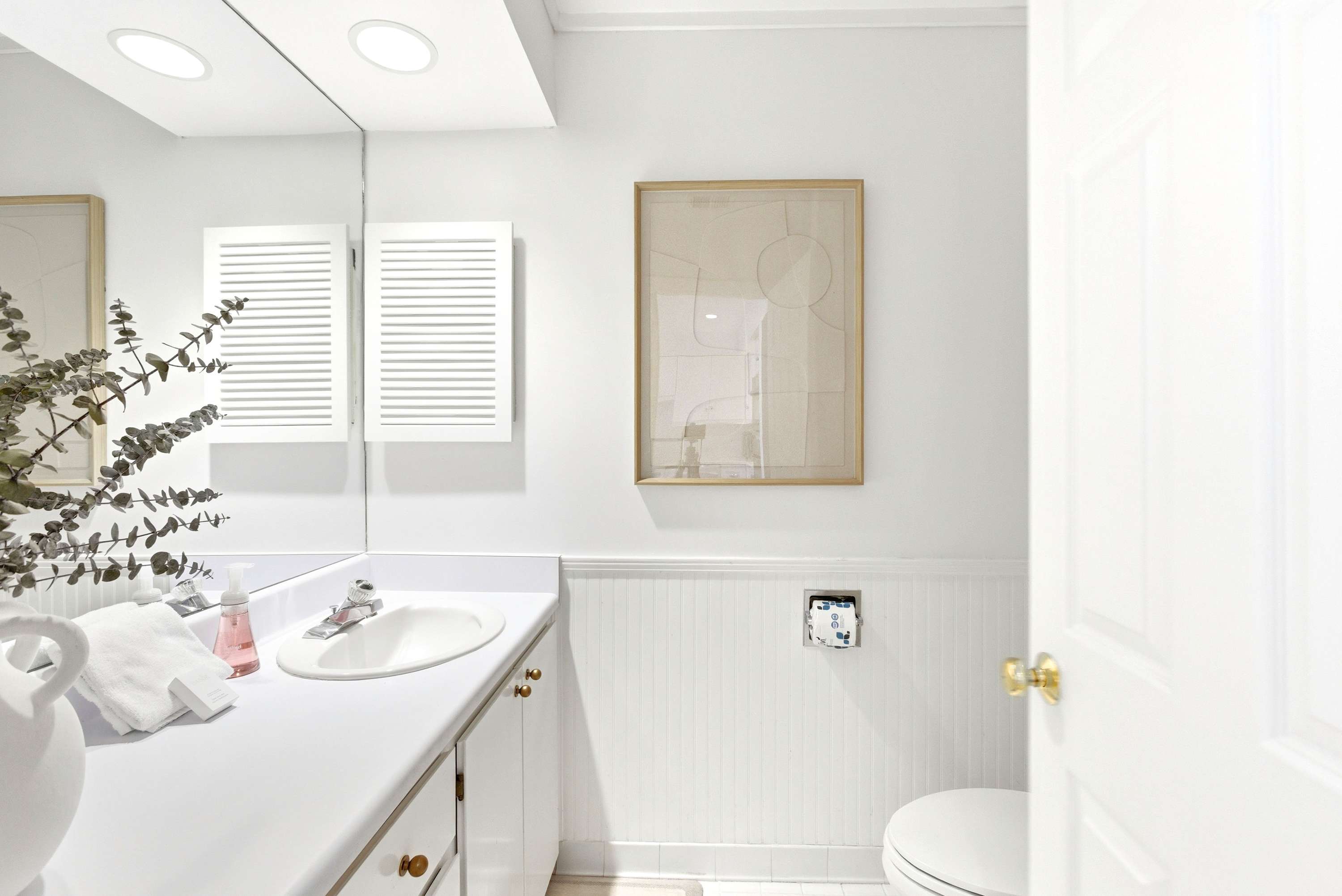 Guest bath with classic bead-board wainscoting, gold hardware, abstract art, and a sprig of fresh eucalyptus.