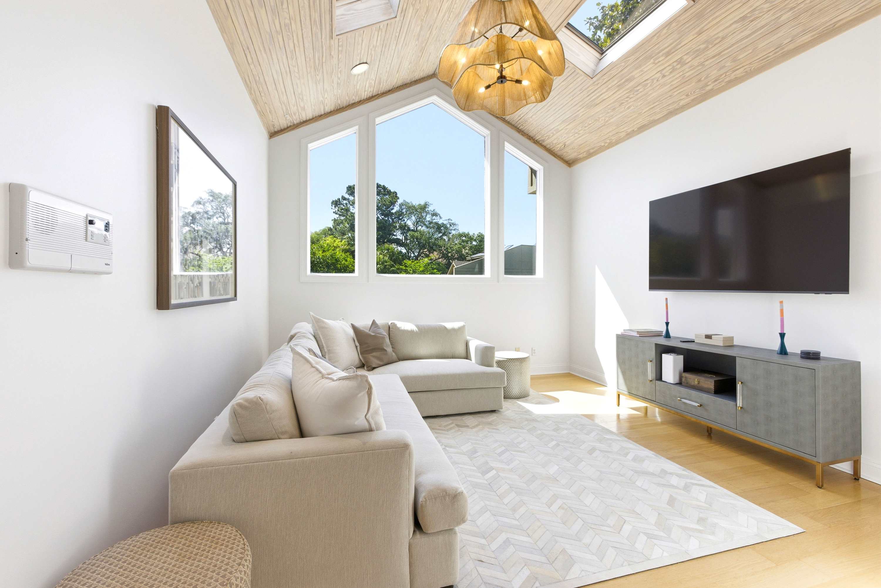 Cathedral wood-plank ceiling with skylights, statement pendant light, and treetop window views define this airy upper-level lounge.