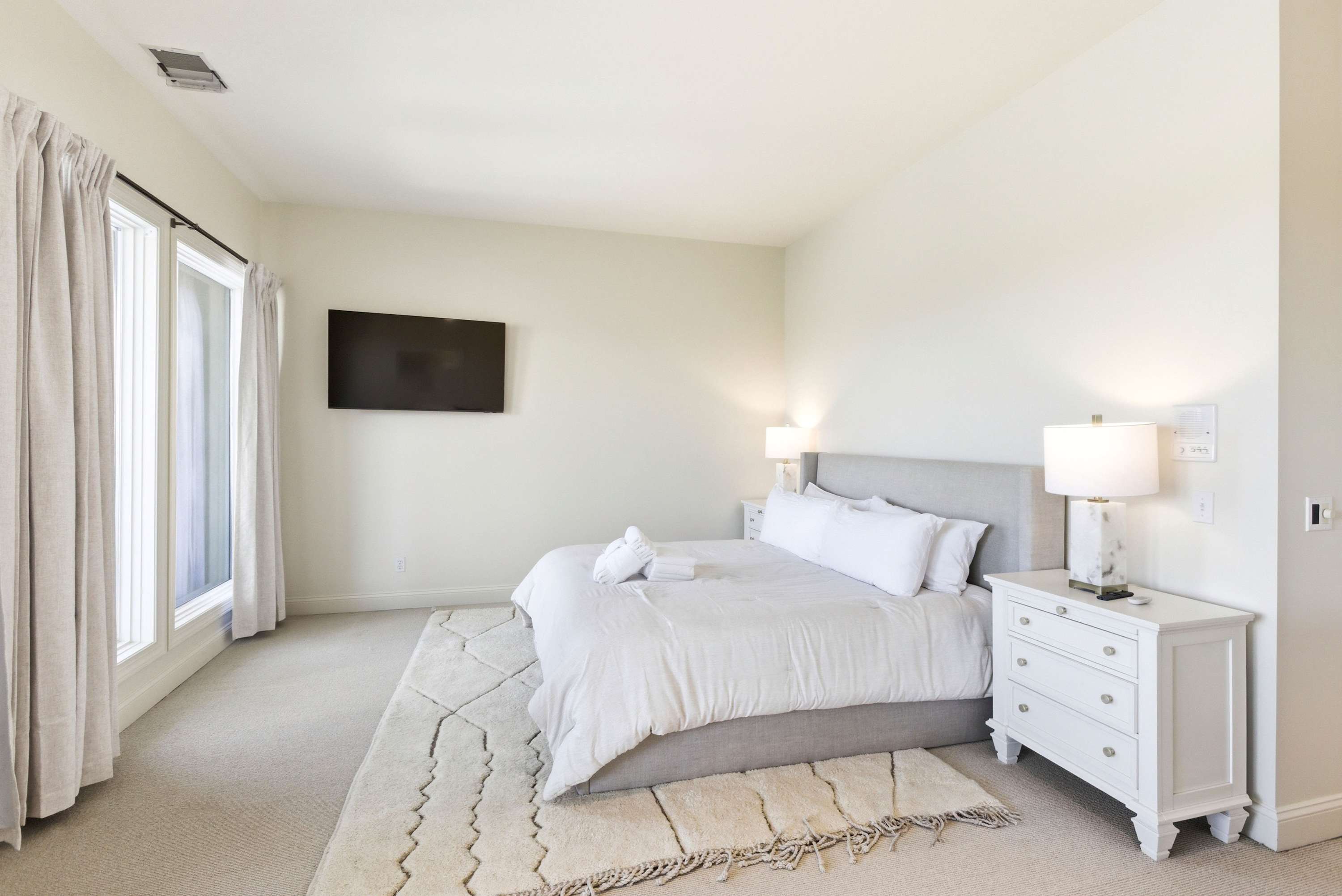 Primary king bedroom with upholstered headboard, dual nightstands, wall-mounted TV, and a Moroccan-inspired area rug.