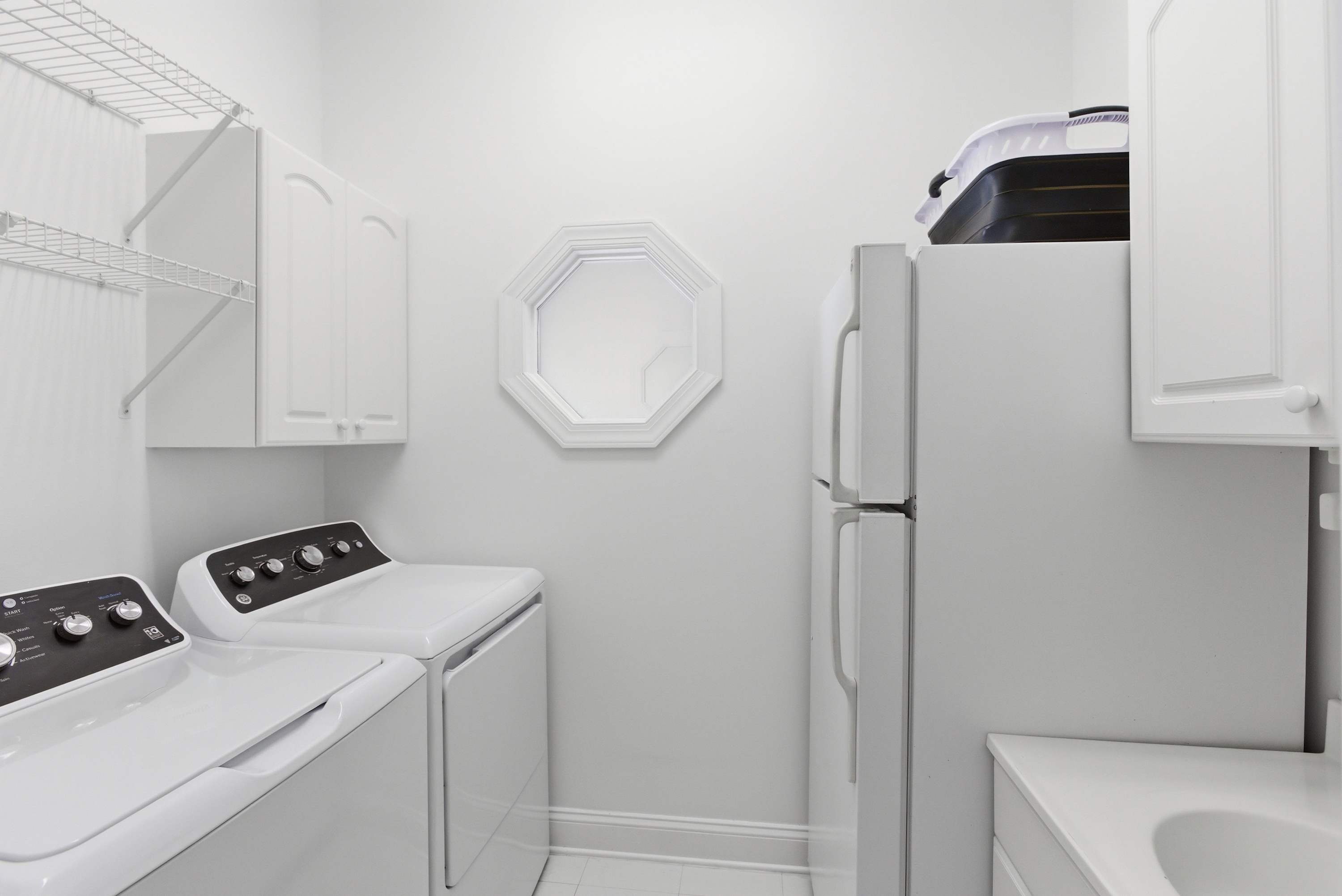 Second-floor laundry room with full-size washer and dryer, extra refrigerator, and abundant white cabinetry.