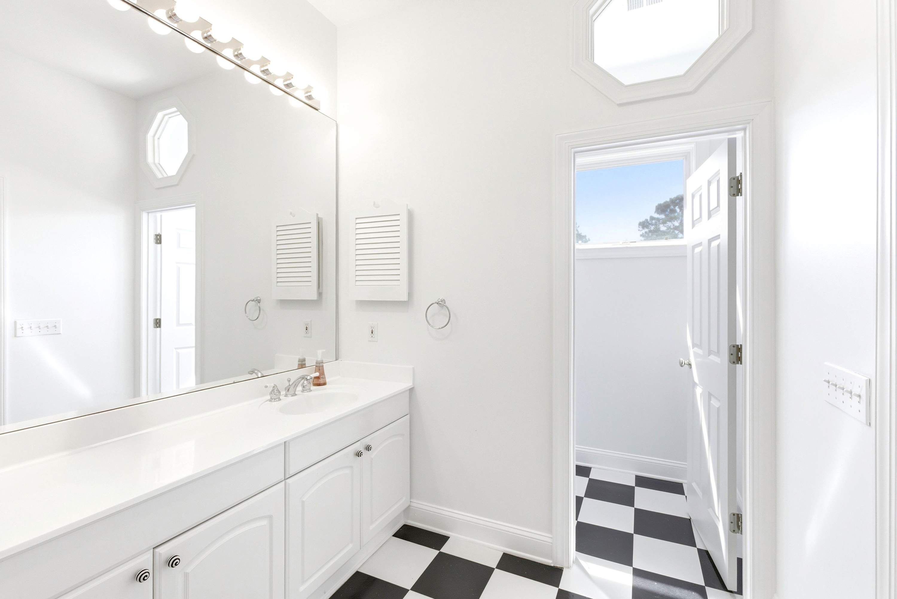 Primary bathroom with dual-sink vanity, separate glass-enclosed shower, and classic checkerboard tile flooring.