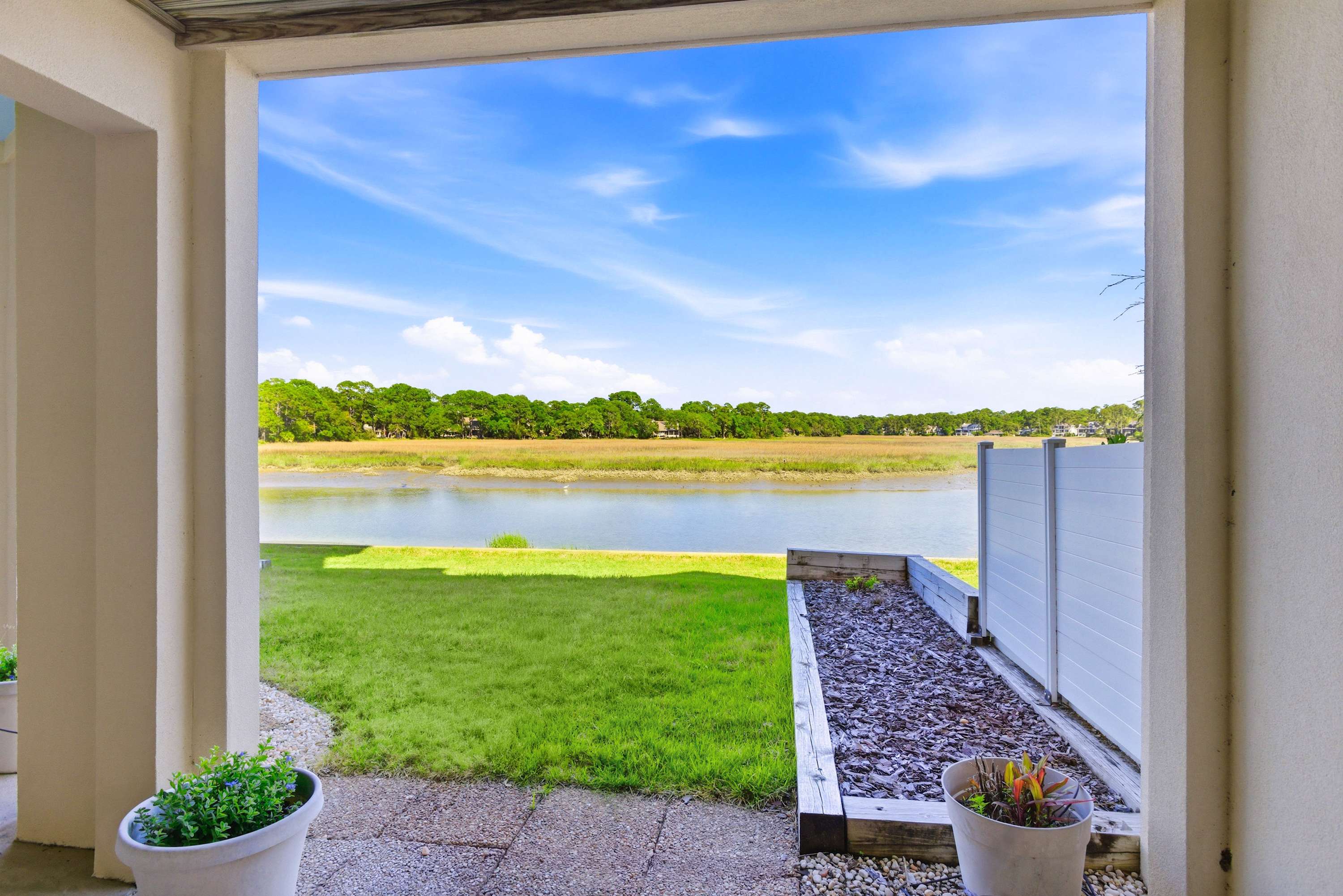 Ground-level covered patio framing a picture-perfect marsh vista, with a lush green lawn leading to the water's edge.