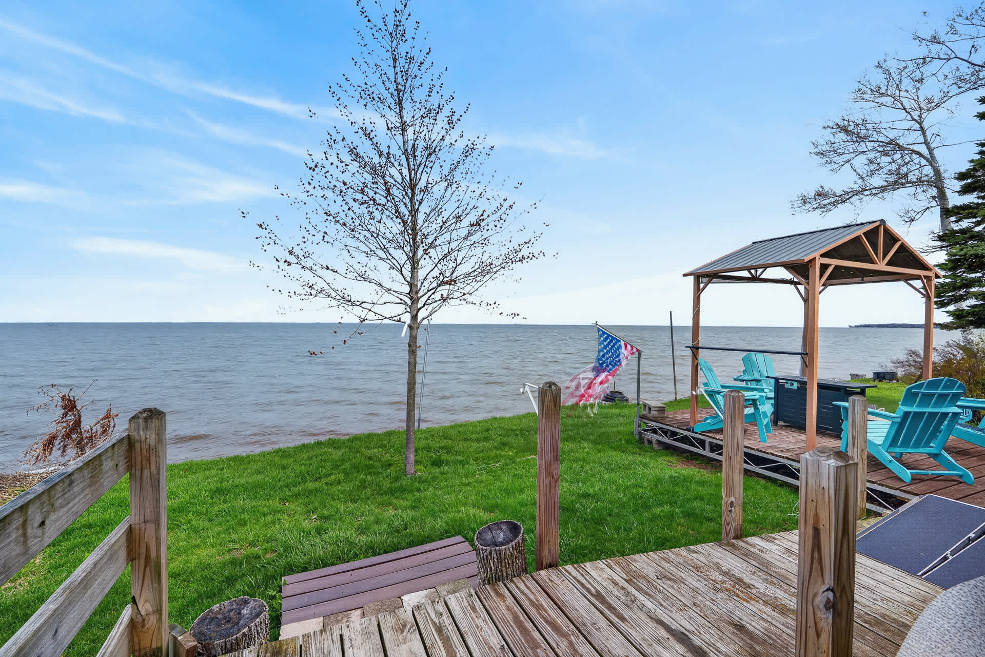 Expansive waterfront property featuring a private gazebo with turquoise seating overlooking serene lake views, complemented by lush green lawn and wooden deck areas for relaxation.