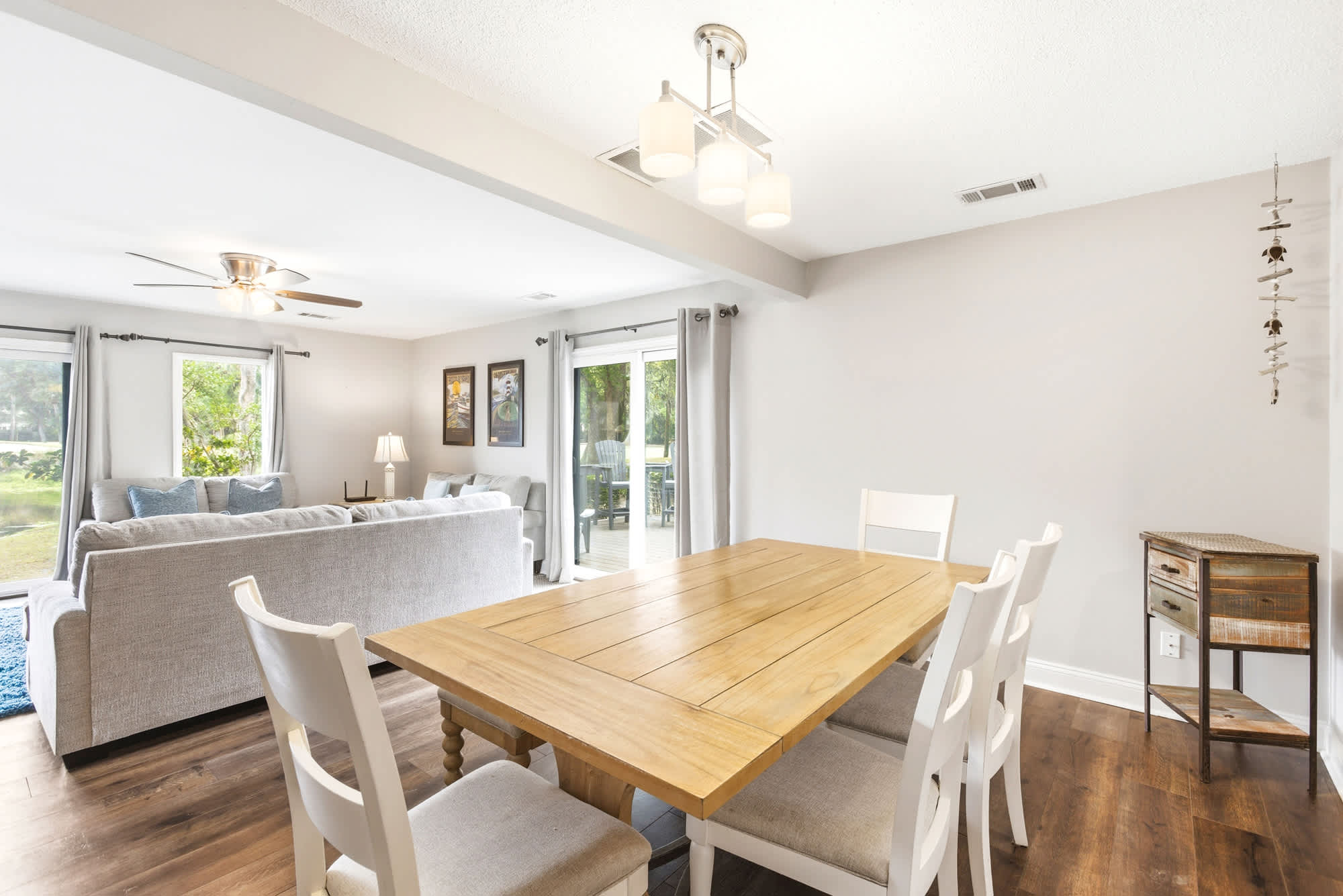 Farmhouse dining table with white chairs, coastal artwork, and a ceiling fan create a relaxed open-plan space perfect for family meals and lazy afternoons.