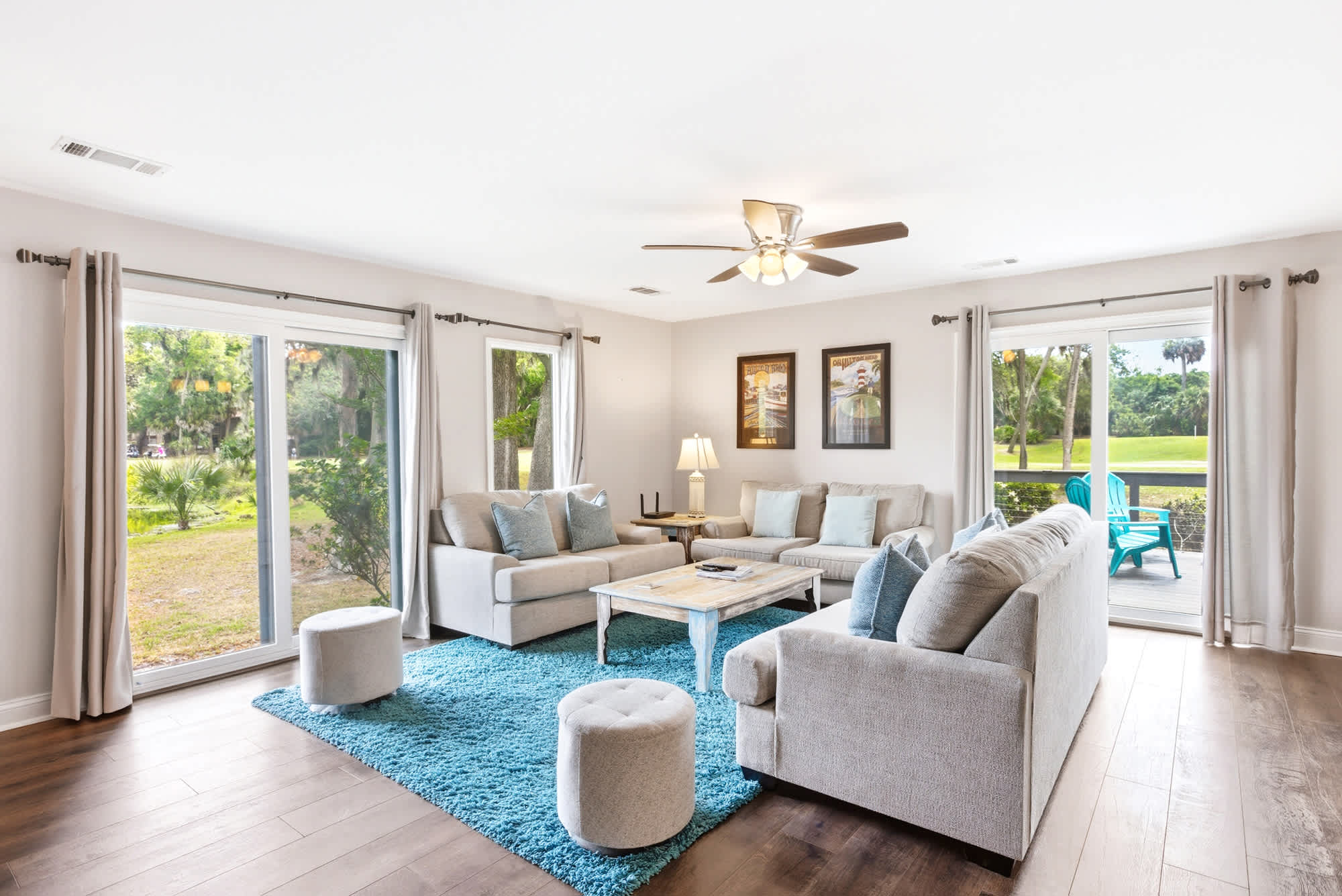 Teal shag rug, gray sectional seating, and sliding glass doors on both sides open the living room to the outdoors, where towering oaks and a serene pond await.