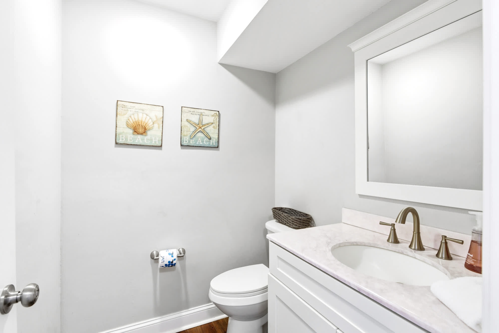 Shell and starfish art, a marble-look vanity, and brushed gold hardware give this powder room an effortlessly coastal touch. (Downstairs)