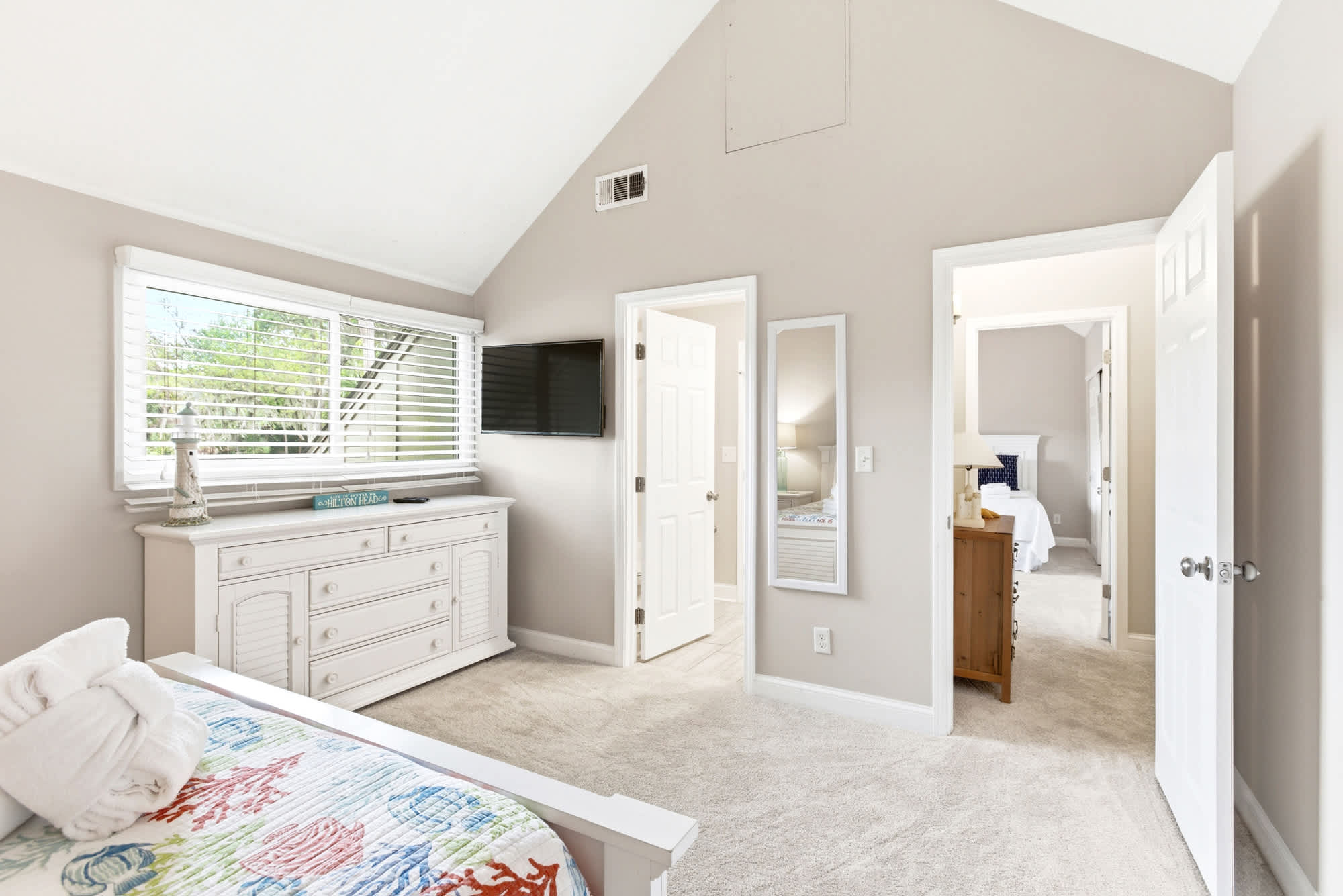 The vaulted ceiling adds volume and airiness to this guest bedroom, complete with TV, dresser, and a full-length mirror.