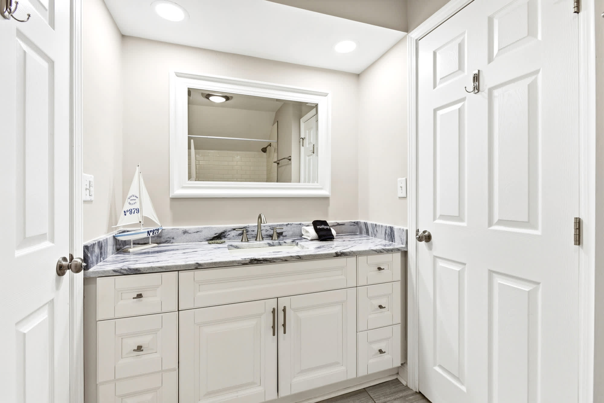 White vanity with a marble-look countertop, sailboat accent, and a framed mirror make this upstairs bath as polished as it is practical.