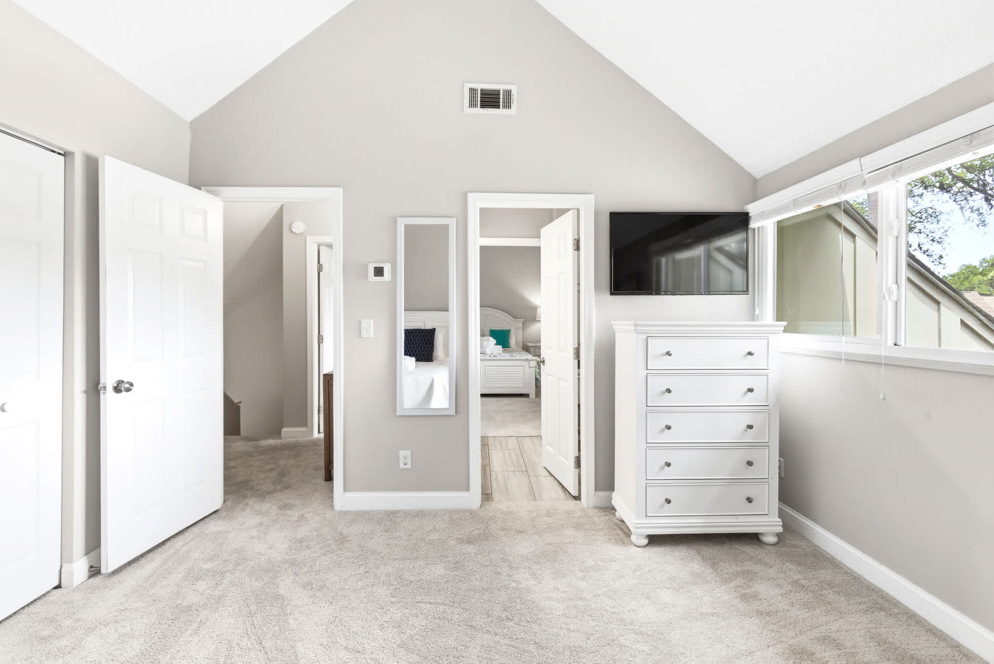 Airy guest bedroom with a TV, dresser, and full-length mirror — a flexible shared space for the whole group.