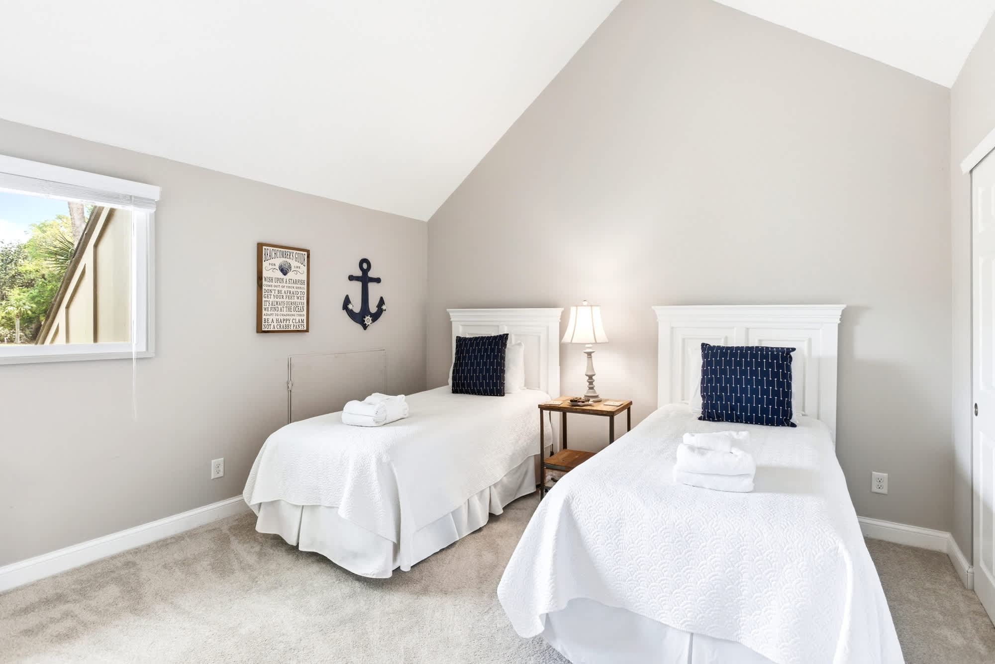 Vaulted ceiling, two white cottage twin beds, navy anchor decor, and a beachcomber's guide sign give this room undeniable coastal charm.