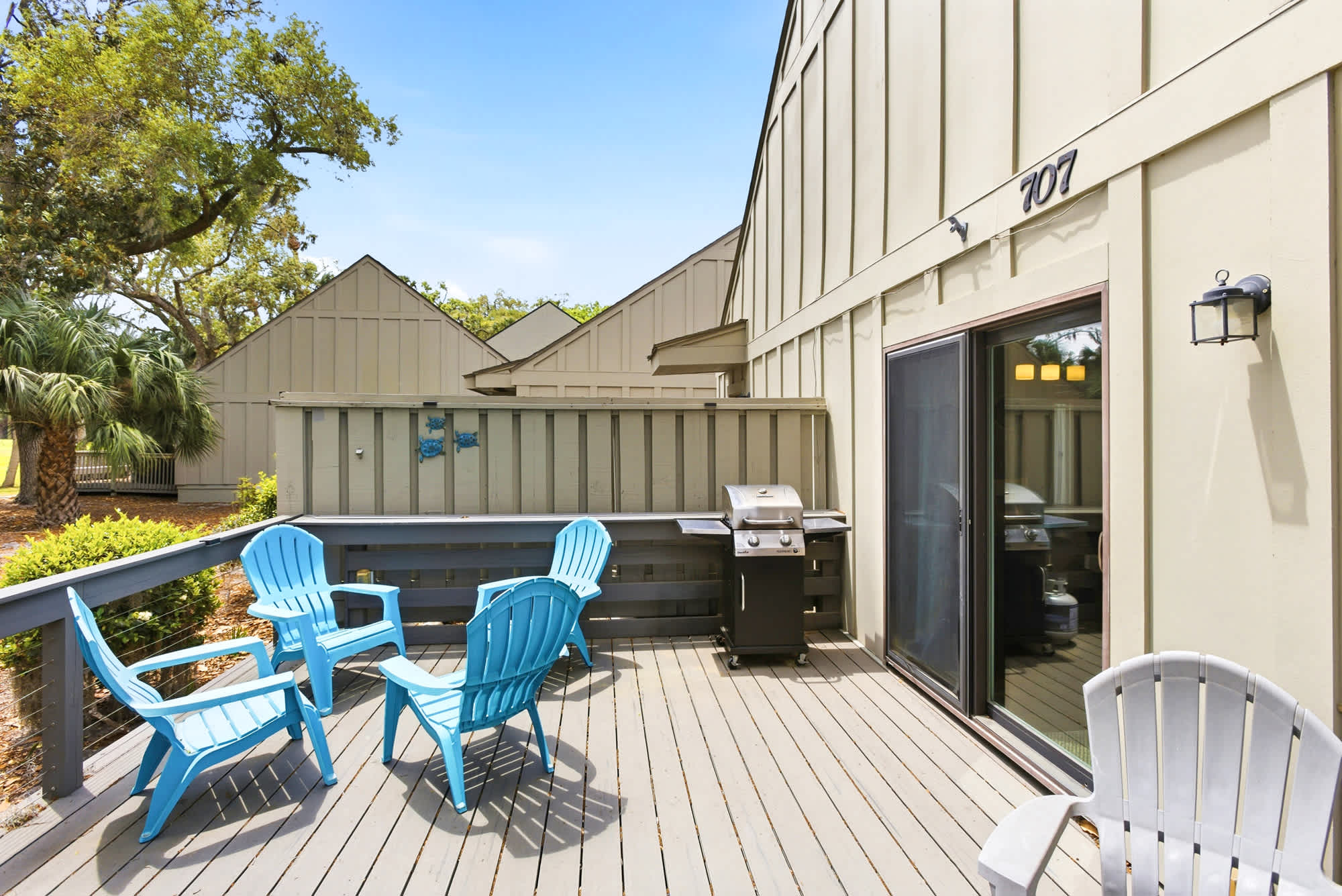 Teal Adirondack chairs, a gas grill, and a casual front deck make outdoor entertaining easy and laid-back.