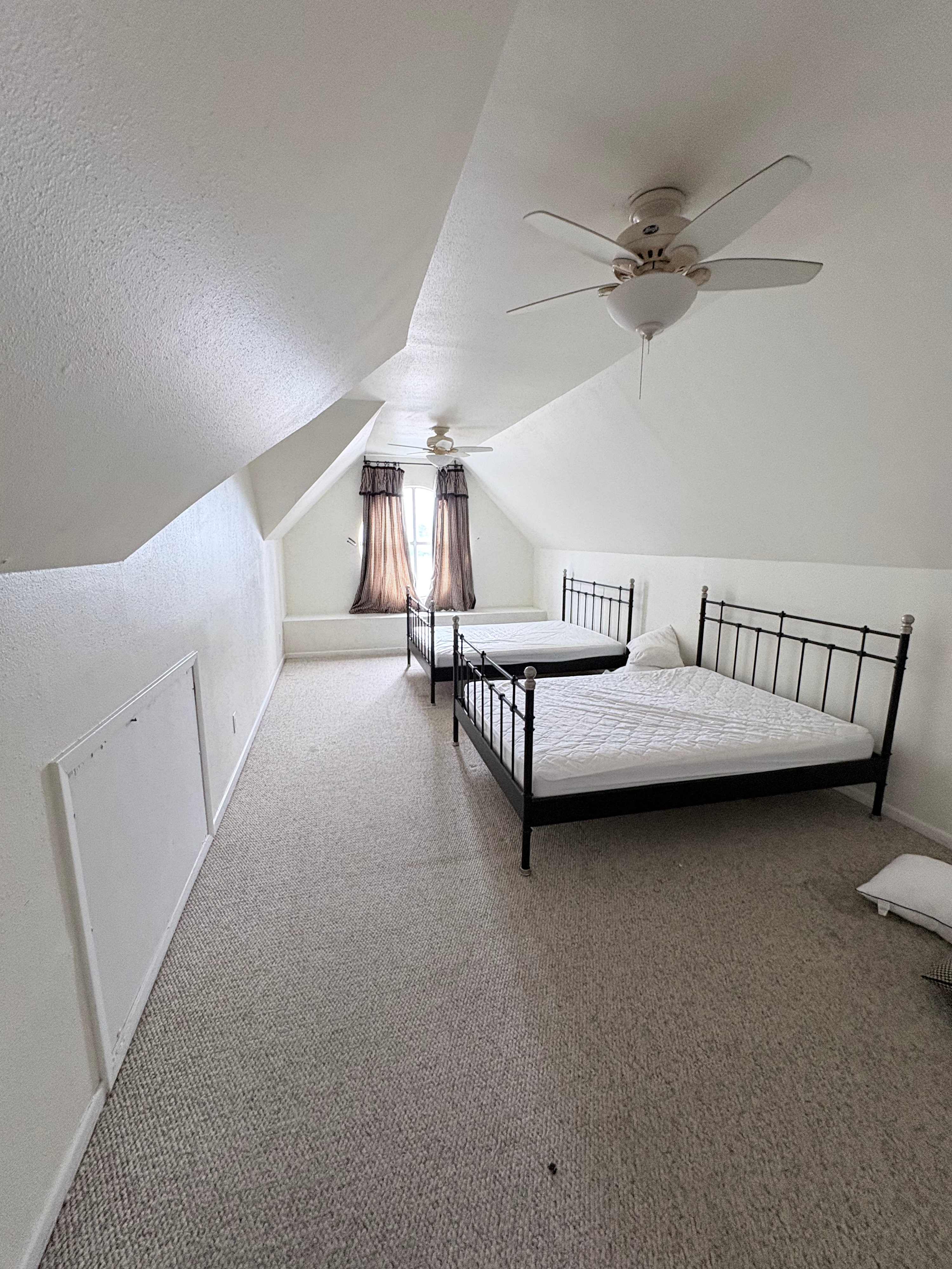 Cozy attic bedroom with twin beds and ceiling fans, perfect for a restful night's sleep.