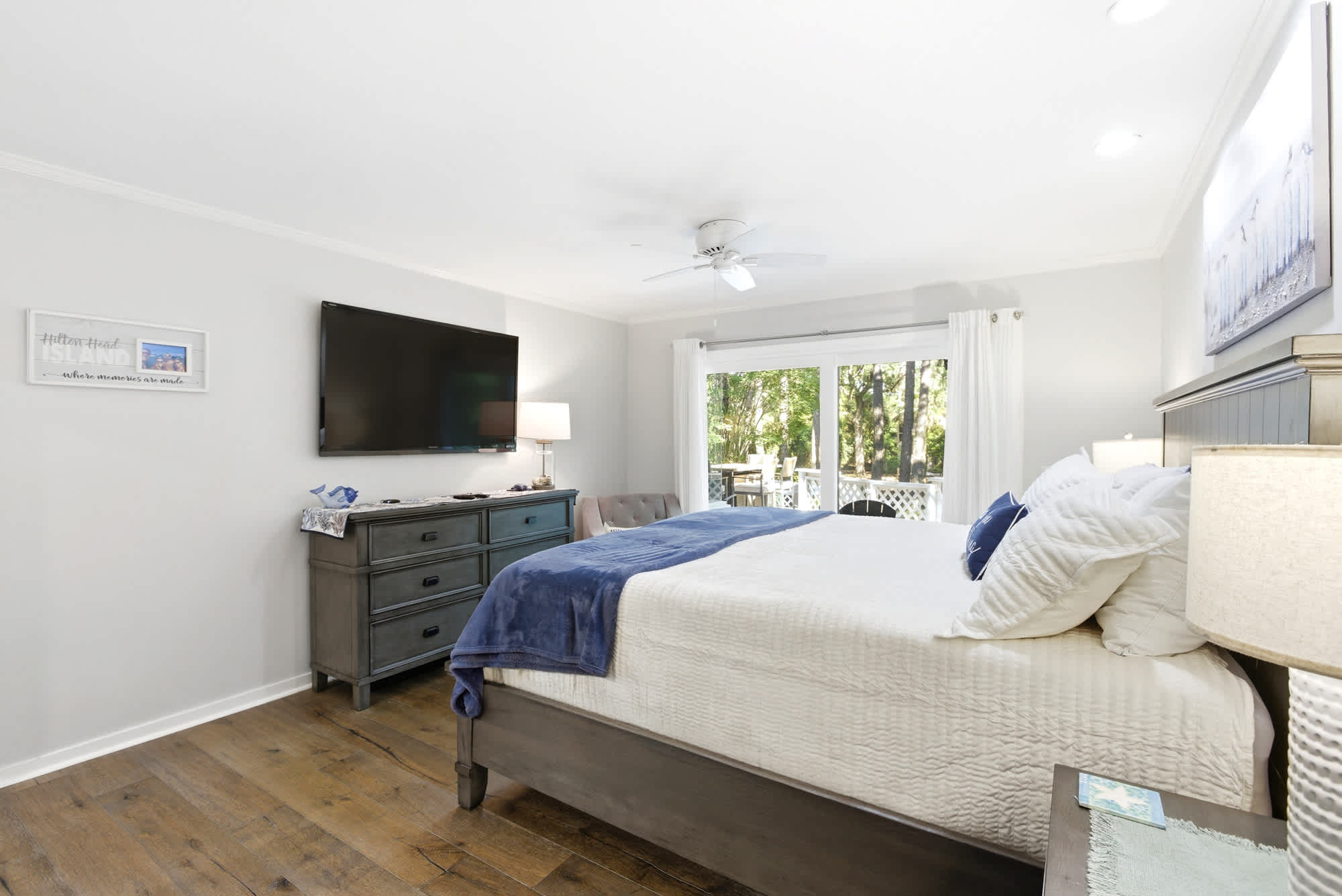 The primary suite's teal dresser, wall-mounted TV, and 'where memories are made' artwork give this room a warm, personal coastal character.