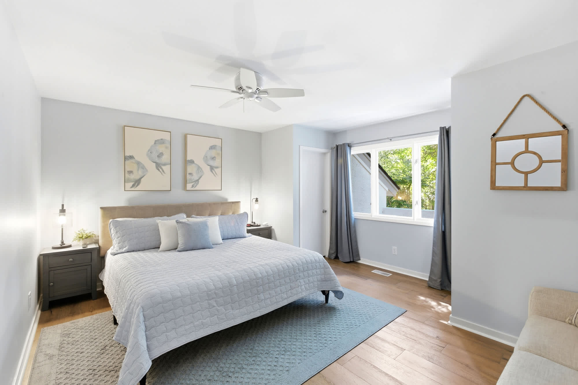 A second king suite in soft coastal blue with textured quilted bedding, fish print art, a rope-frame mirror, and warm hardwood floors.