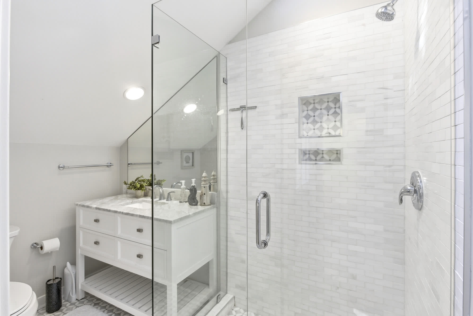 A standout guest bath with floor-to-ceiling marble tile, a frameless glass walk-in shower, mosaic accent niches, and a crisp white vanity.