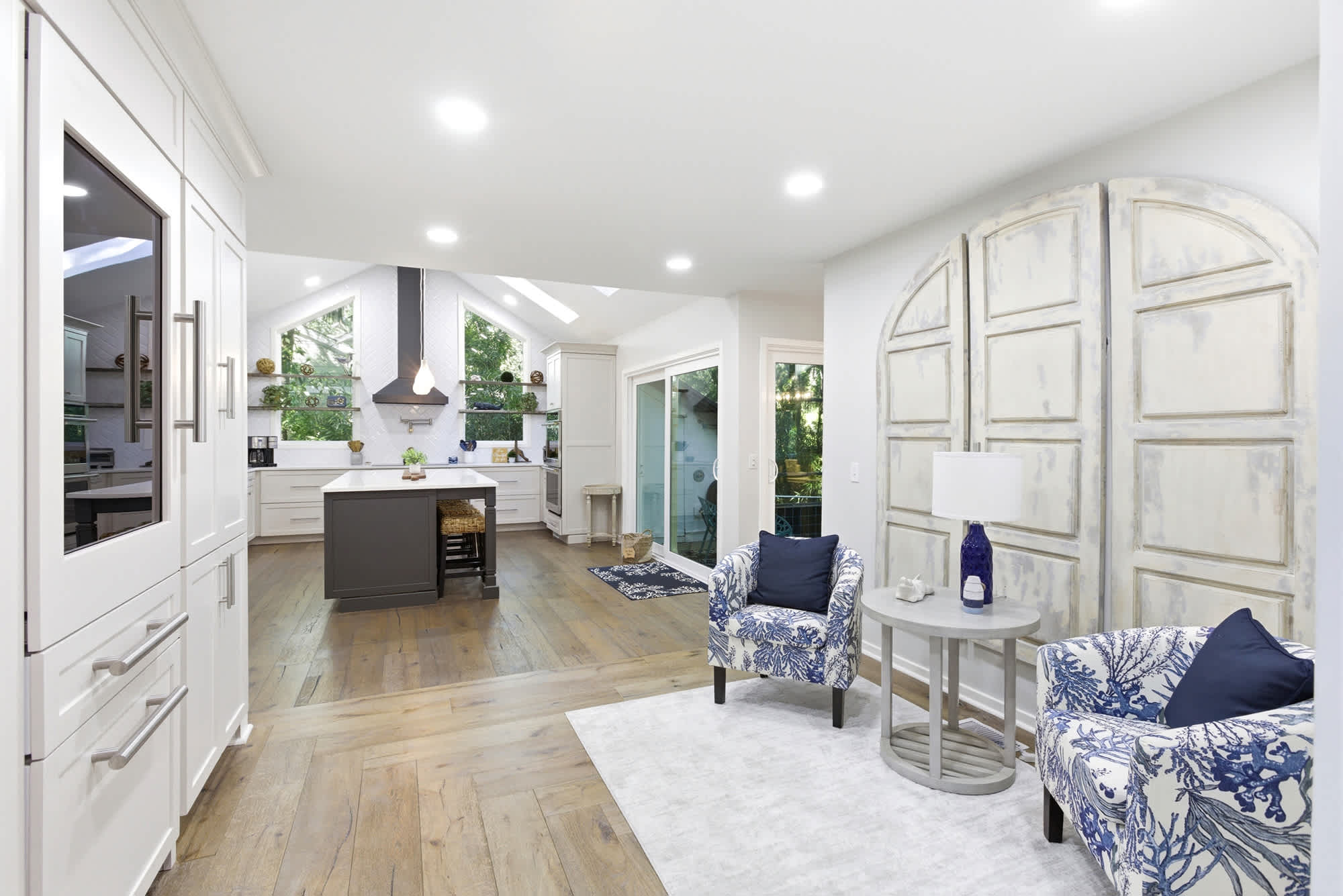White custom cabinetry, a charcoal center island, and blue-and-white coral print accent chairs beside a dramatic distressed arch installation make this kitchen-nook one of a kind.