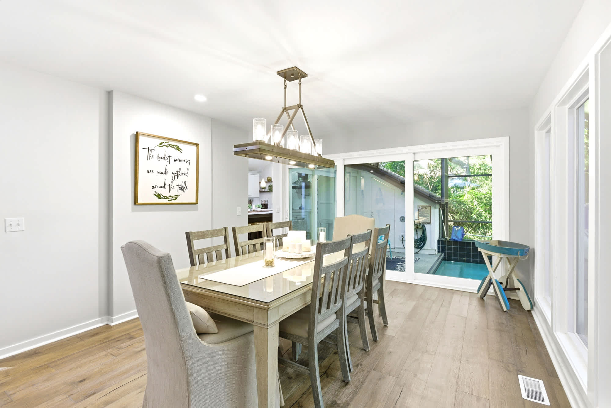The eight-seat dining table sits beneath a gold chandelier with pool and screened enclosure views through the sliding glass doors — the ideal setting for every evening meal.