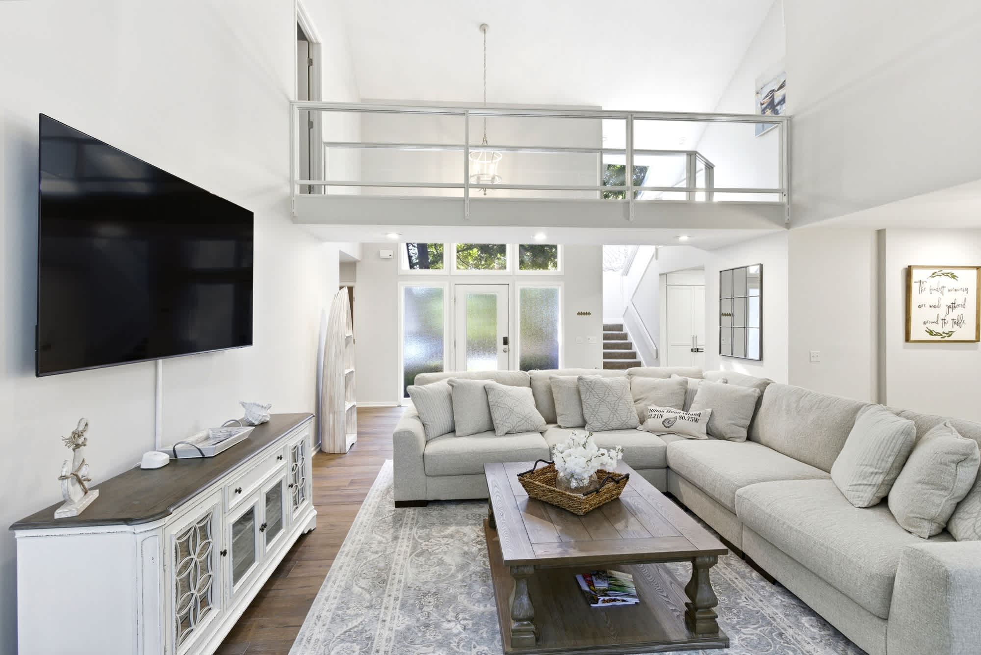 The full living room reveals the entry's frosted glass doors, the staircase rising to the loft, and the glass railing above — an airy, architecturally impressive space.
