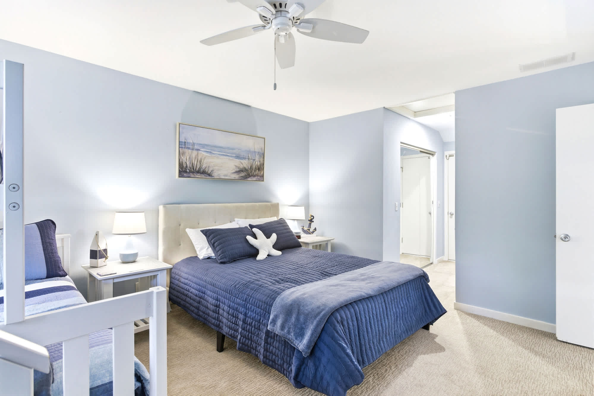 A closer look at the queen bed in this blue-walled retreat, with soft lighting, coastal nightstands, and easy access to the closet hallway.