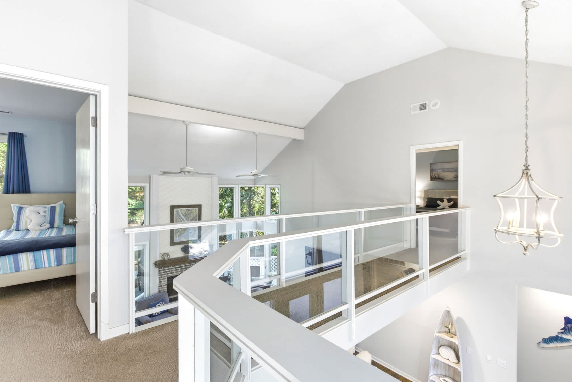 The upper loft hallway with glass-panel railing overlooks the living room below, connecting all the upstairs bedrooms under a dramatic vaulted ceiling.